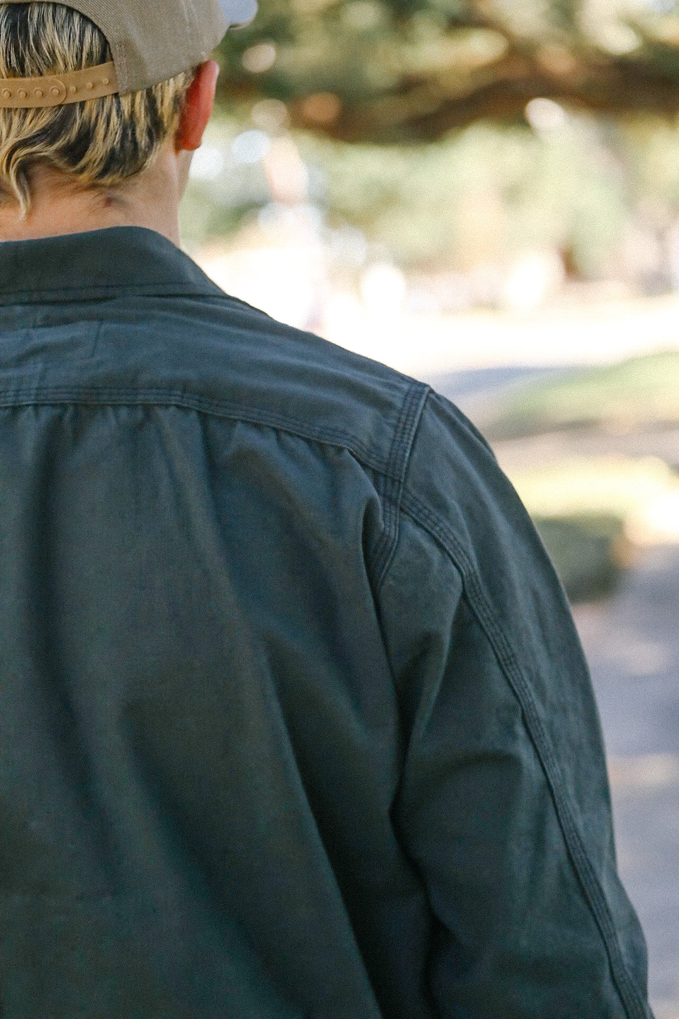 Back view of person wearing dark green jacket and beige cap in outdoor casual setting