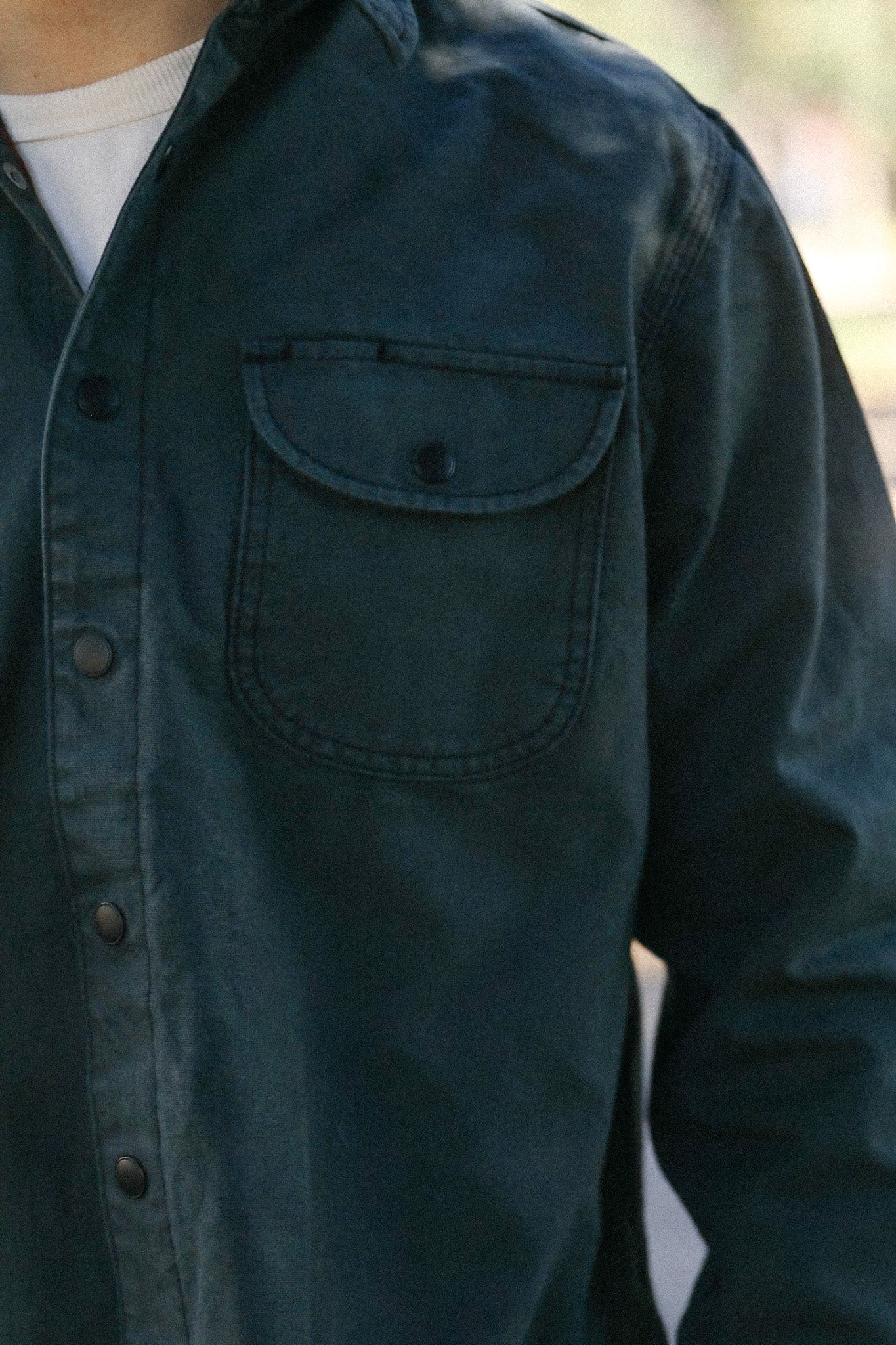 close-up of dark green button-up work jacket with chest pocket and snap buttons, layered over white shirt