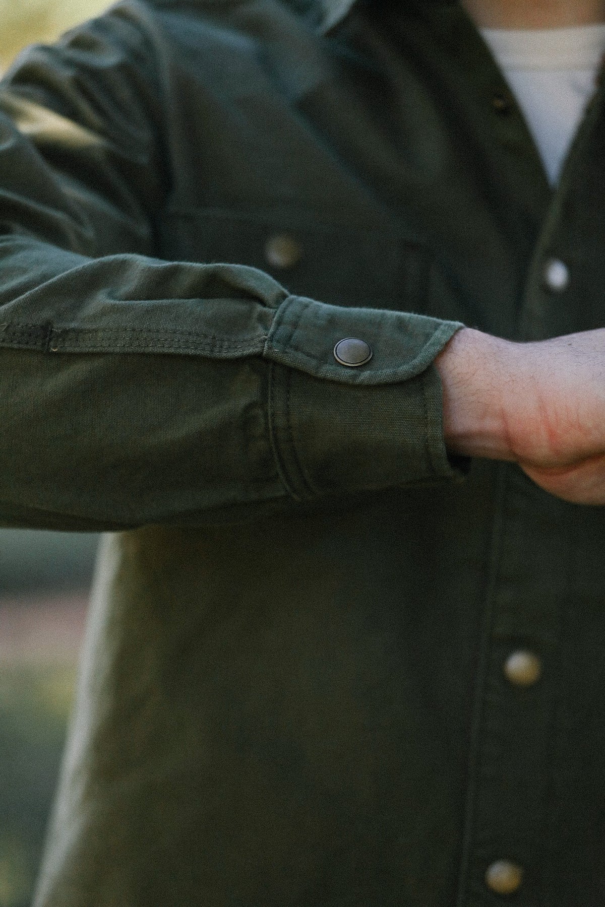 Close-up of green work shirt cuff with metal snap button on a person's wrist from Iron Shop Provisions