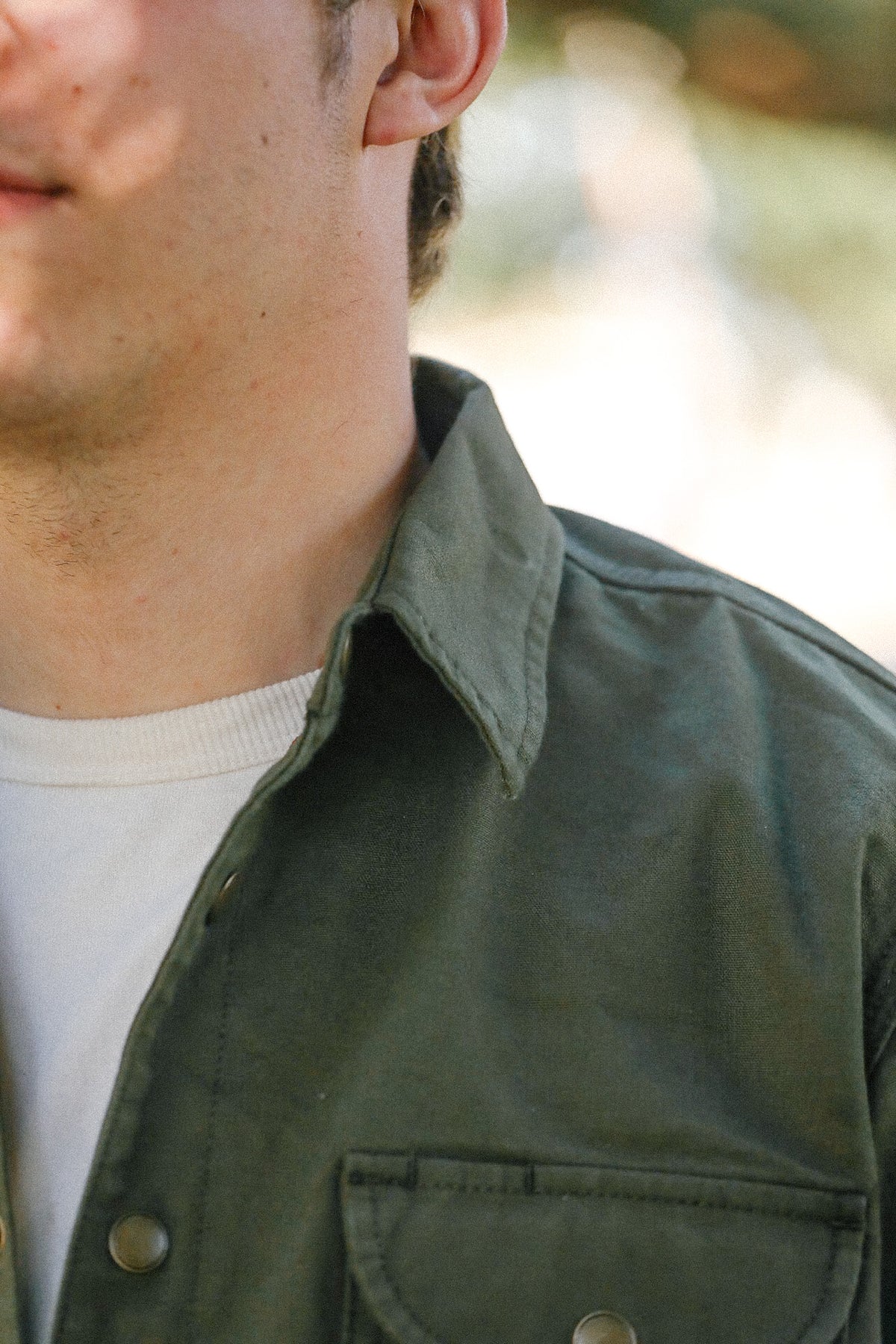 Close-up of man wearing olive green button-up shirt with chest pocket over white t-shirt