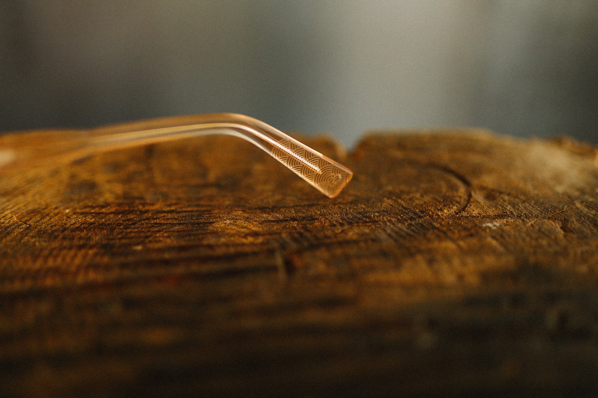 Close-up of a clear, curved glass pipe with intricate etched patterns resting on a rustic wooden surface