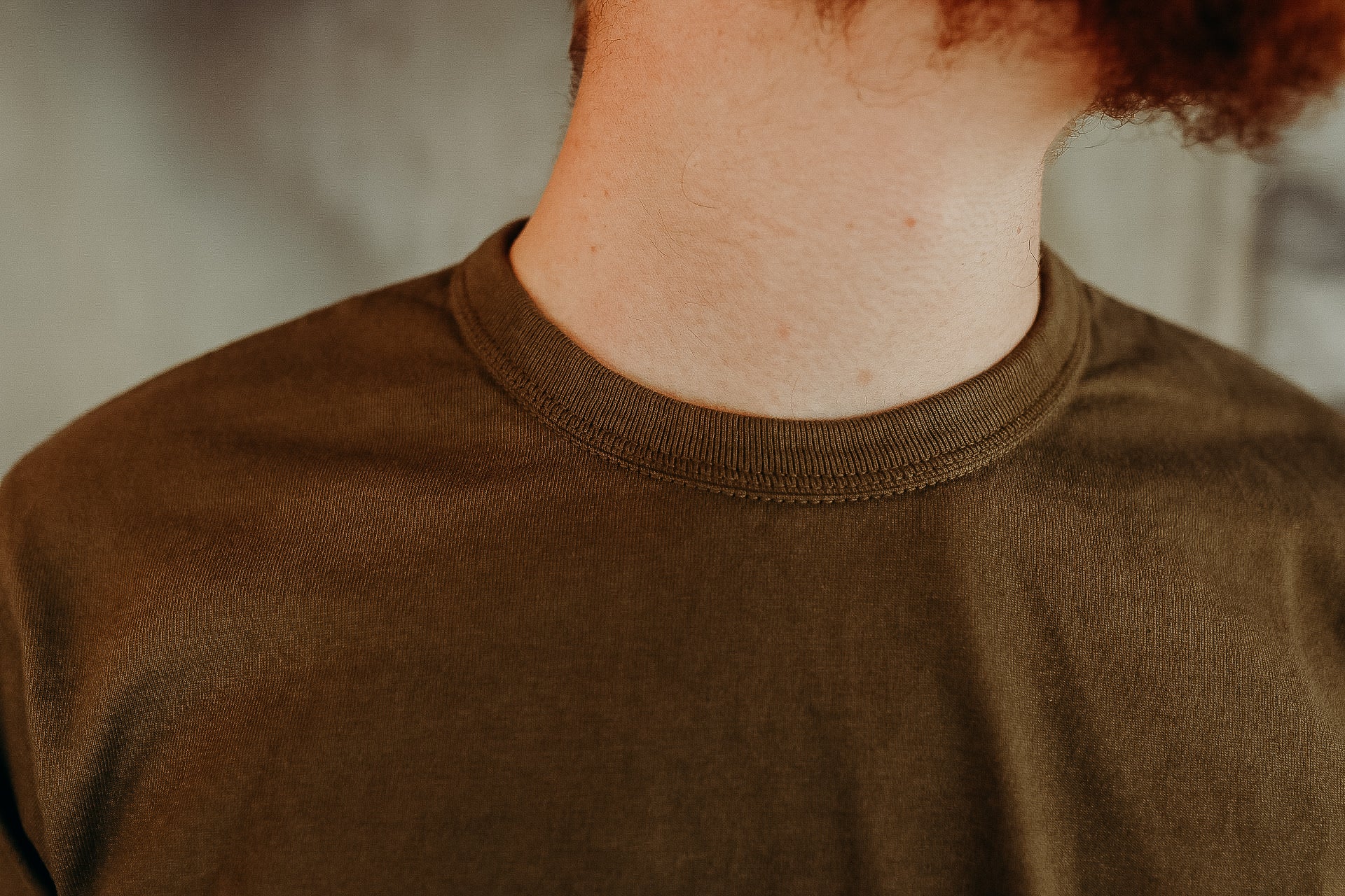 Close-up of a person wearing an olive green crewneck t-shirt showing fabric texture and neckline detail