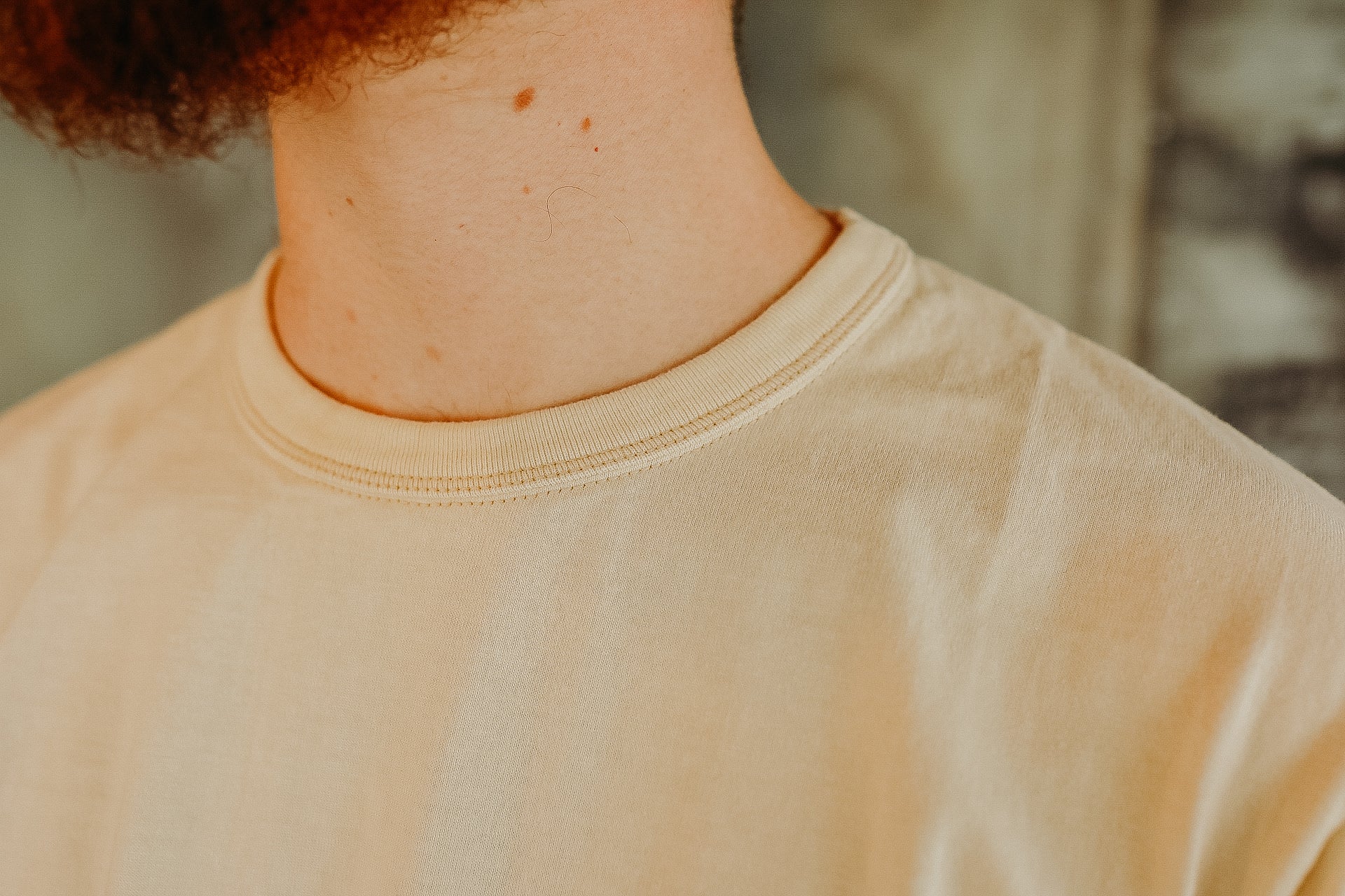 Close-up of a person's neck and beige crew neck t-shirt with soft fabric texture
