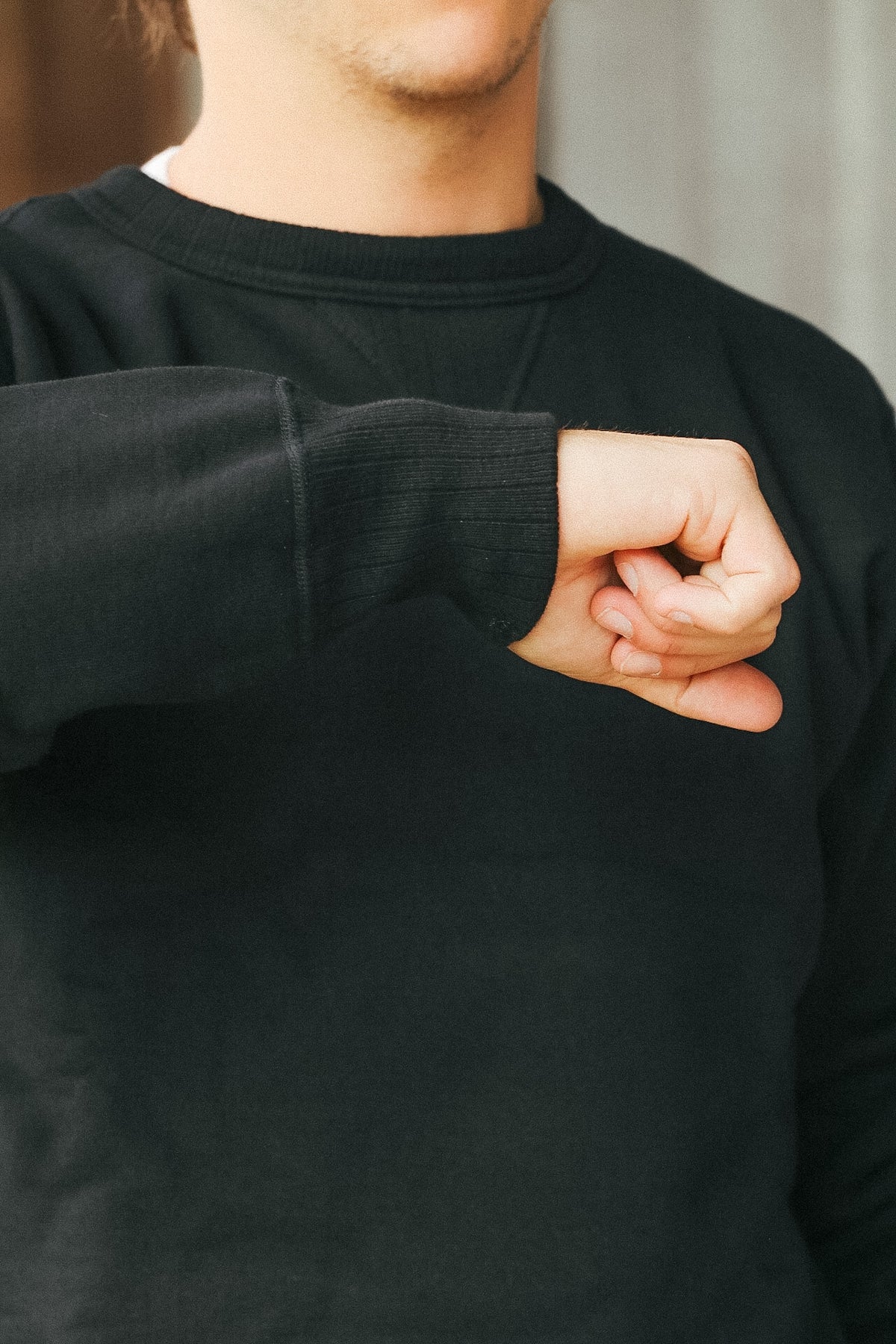 A close-up of a person wearing a black crewneck sweatshirt, showing the ribbed sleeve cuff and the front of the garment.