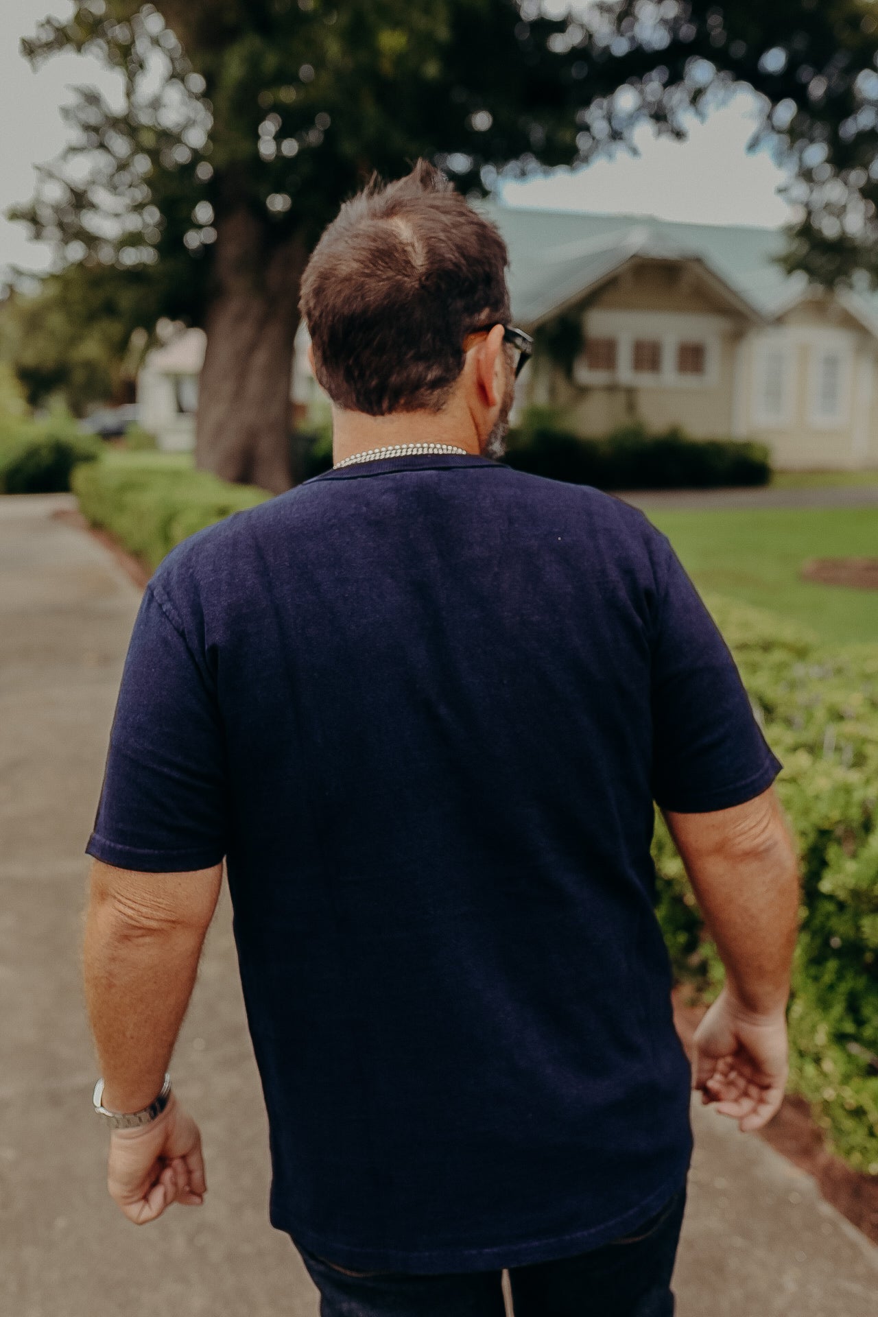 Man wearing navy blue t-shirt walking on path near hedge with house in background