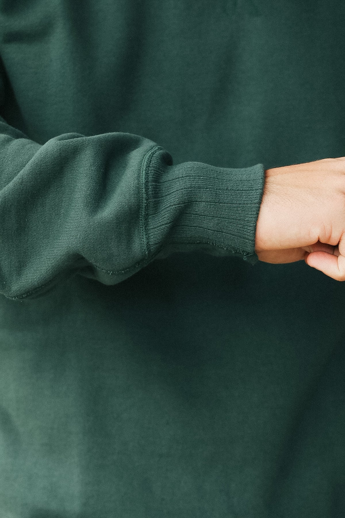 Close-up of a person wearing a dark forest green ribbed knit sweater, showing the sleeve cuff and hand.