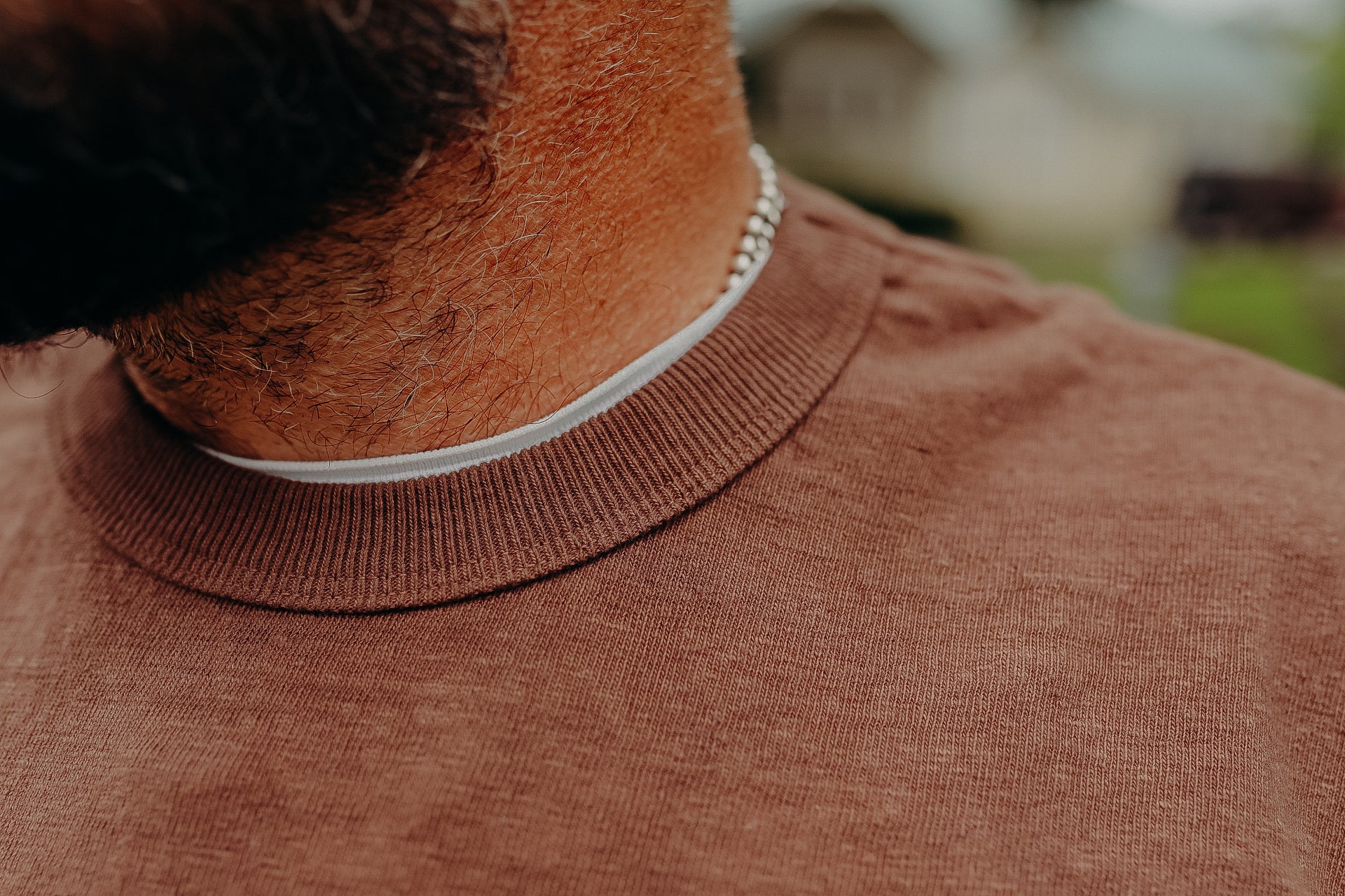 Close-up of a man wearing a brown crewneck sweater layered over a white t-shirt, showcasing casual men's fashion