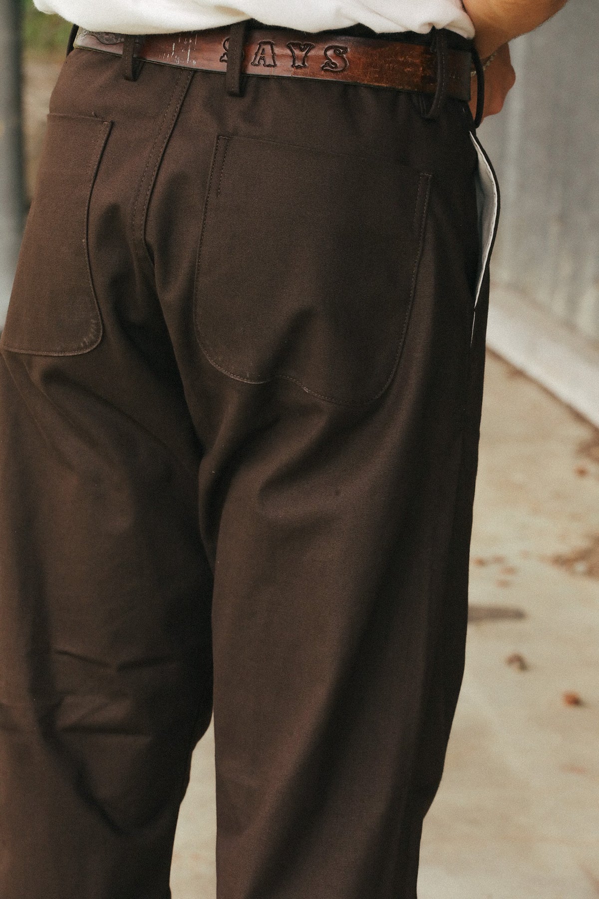 Close-up back view of a person wearing dark brown canvas work pants with a brown leather belt, standing outdoors.