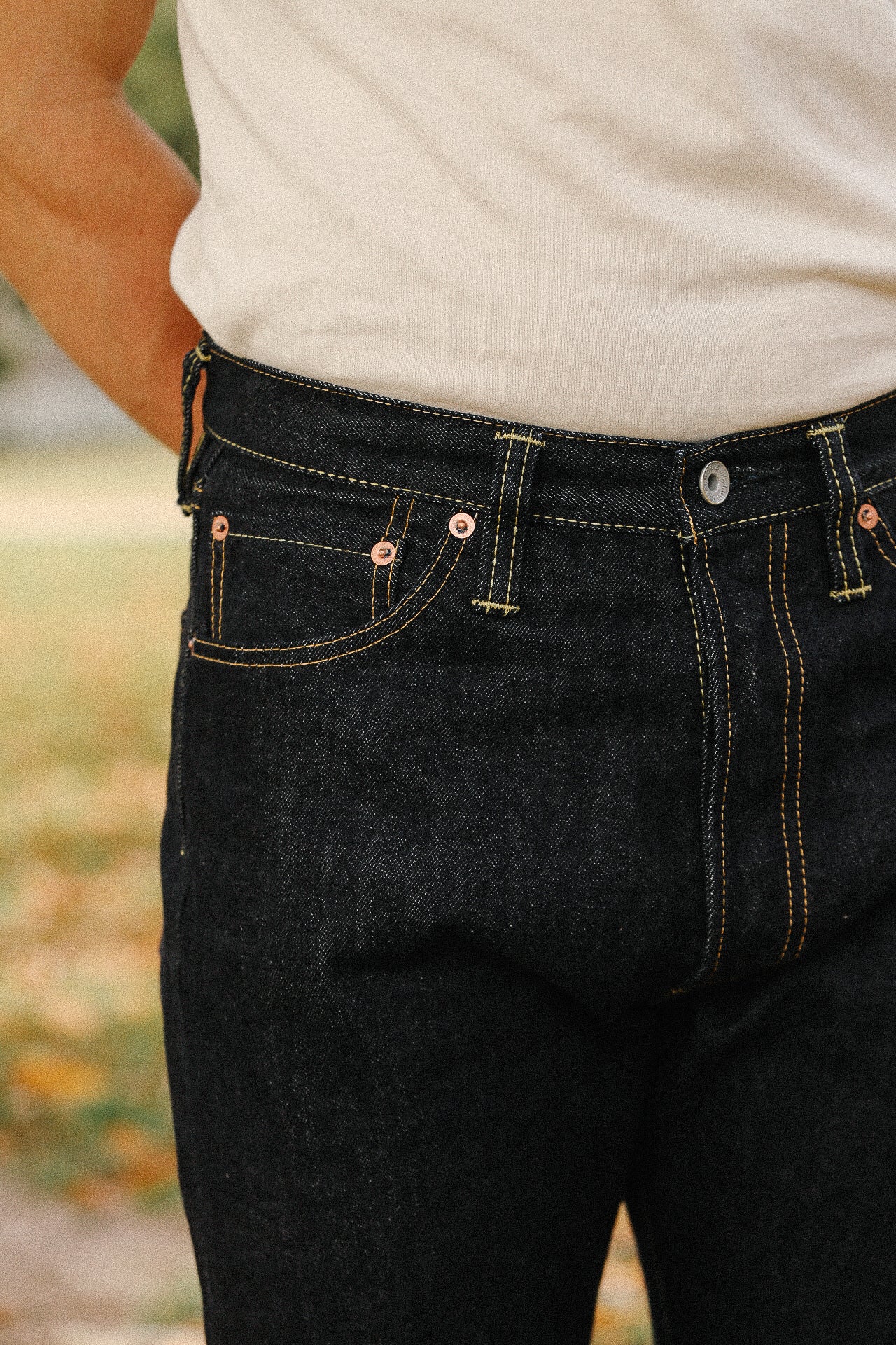 Close-up of person wearing black raw denim jeans with contrast stitching and a white shirt
