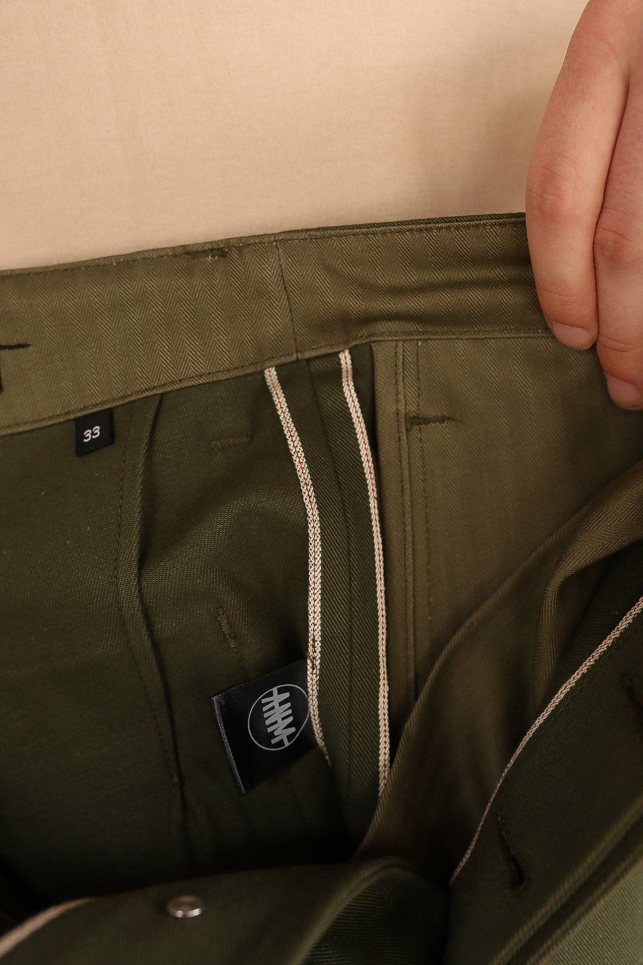 Close-up of olive green pants waistband with selvedge details and size tag 33 inside