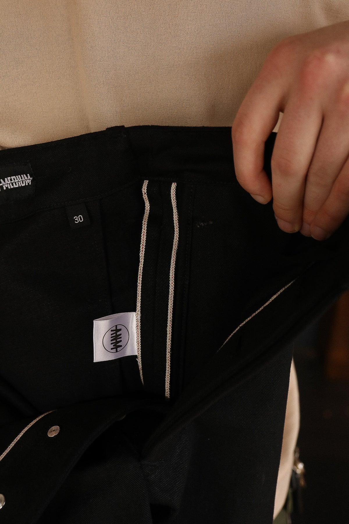 Close-up of black selvedge denim jeans inside view with size 30 tag and hand holding waistband