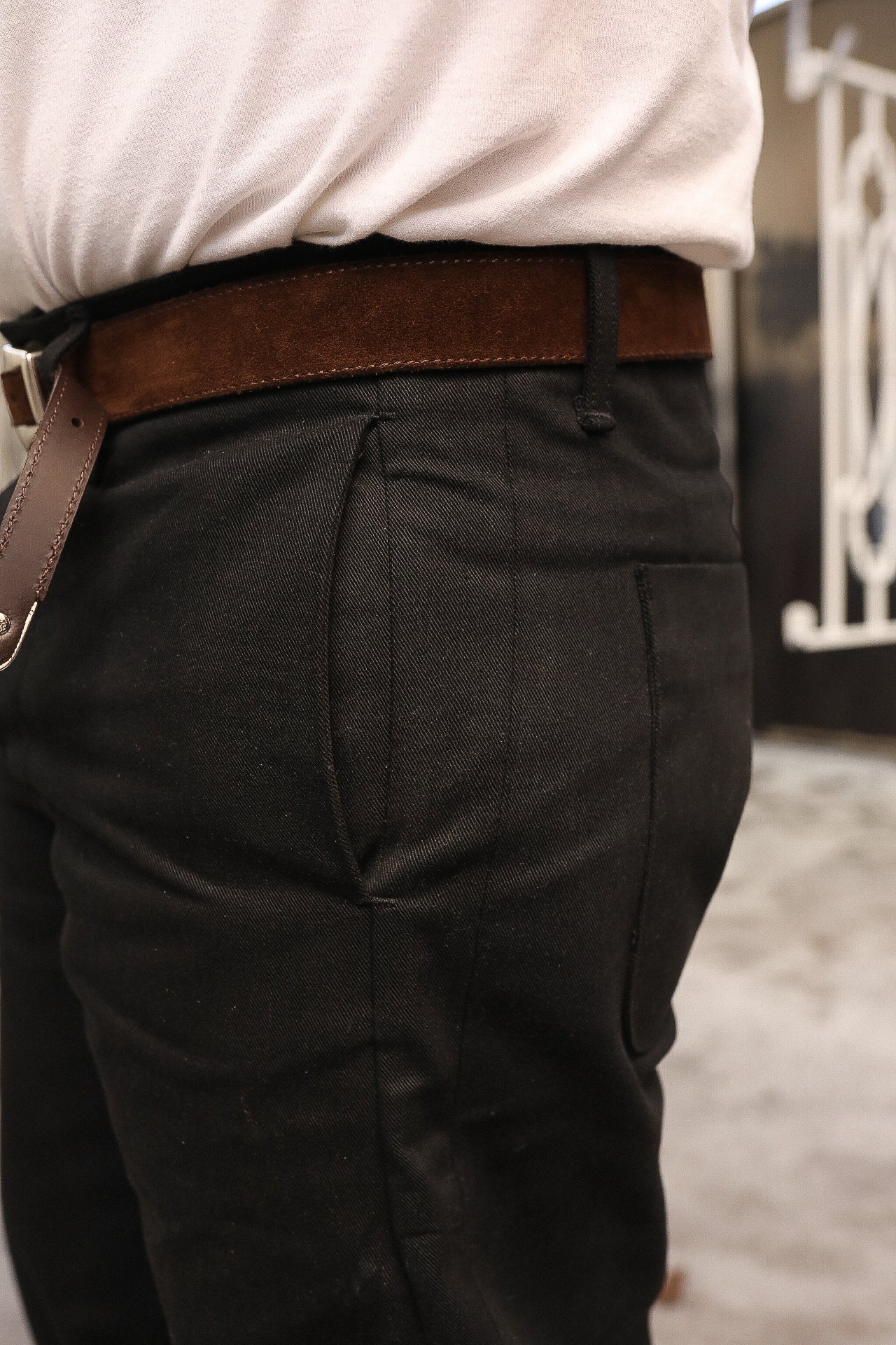 Close-up of person wearing black pants with brown suede belt and tucked light beige shirt