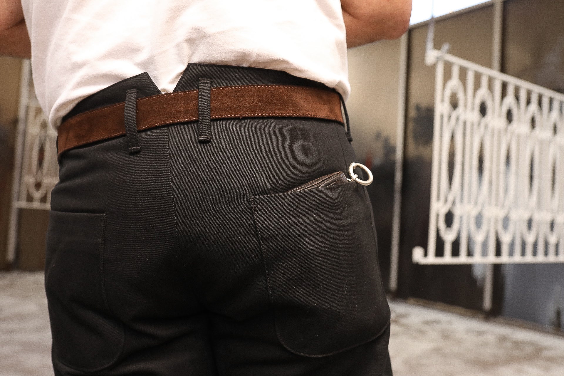 Person wearing black pants with a brown suede belt and a keychain visible in back pocket