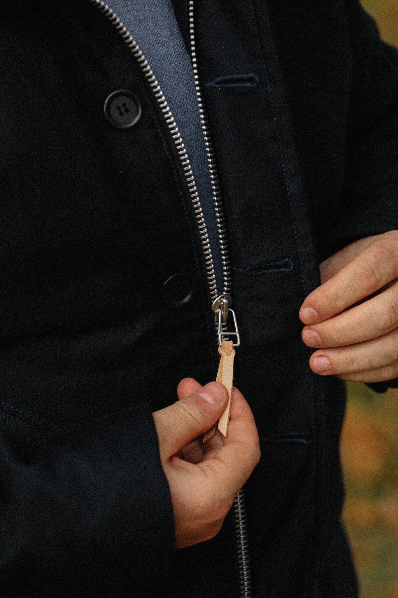 Close-up of hands zipping a dark jacket with leather pull tab on a metal zipper
