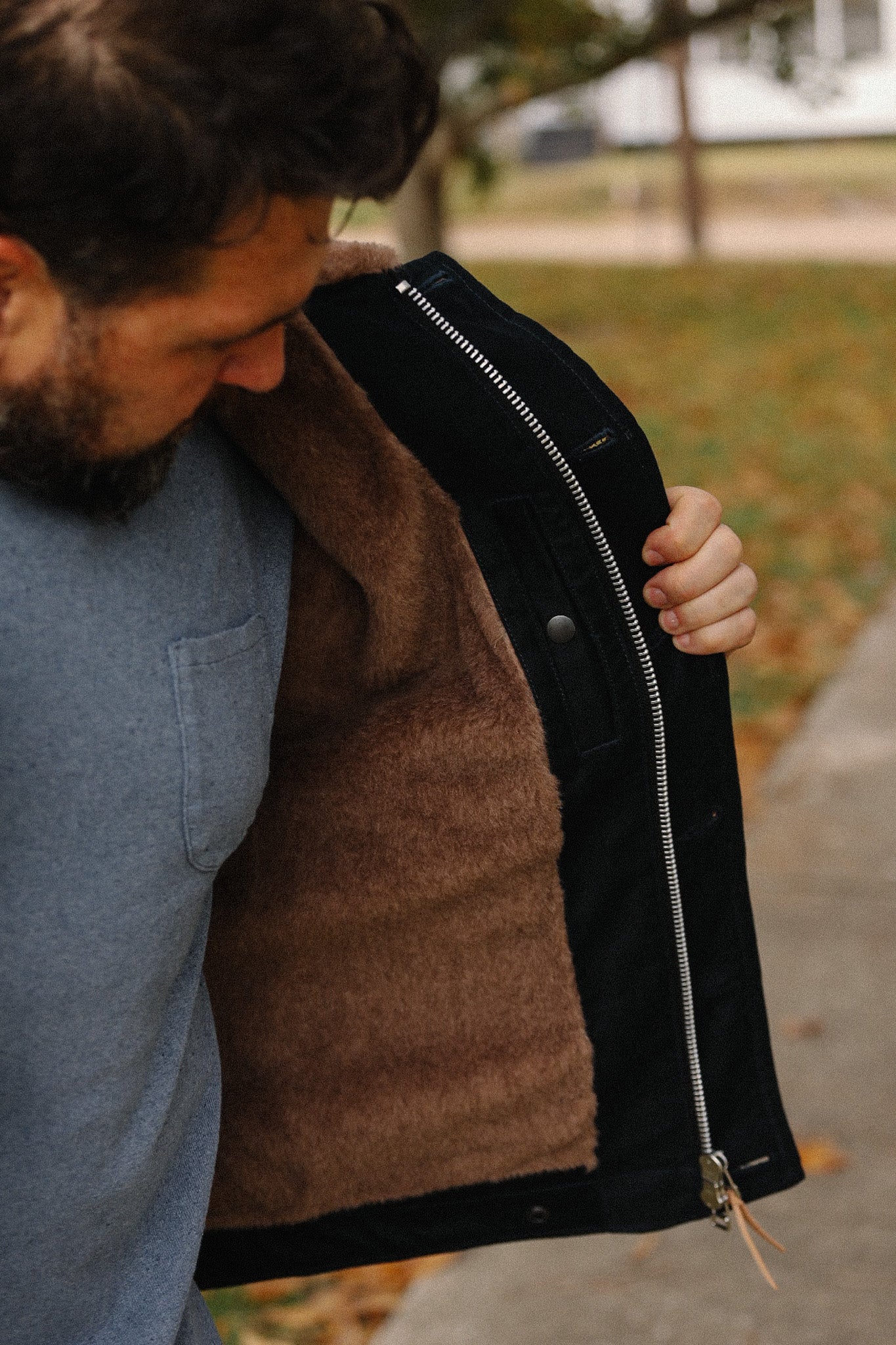 Man showing interior of black jacket with brown fleece lining and silver zipper outdoors in autumn