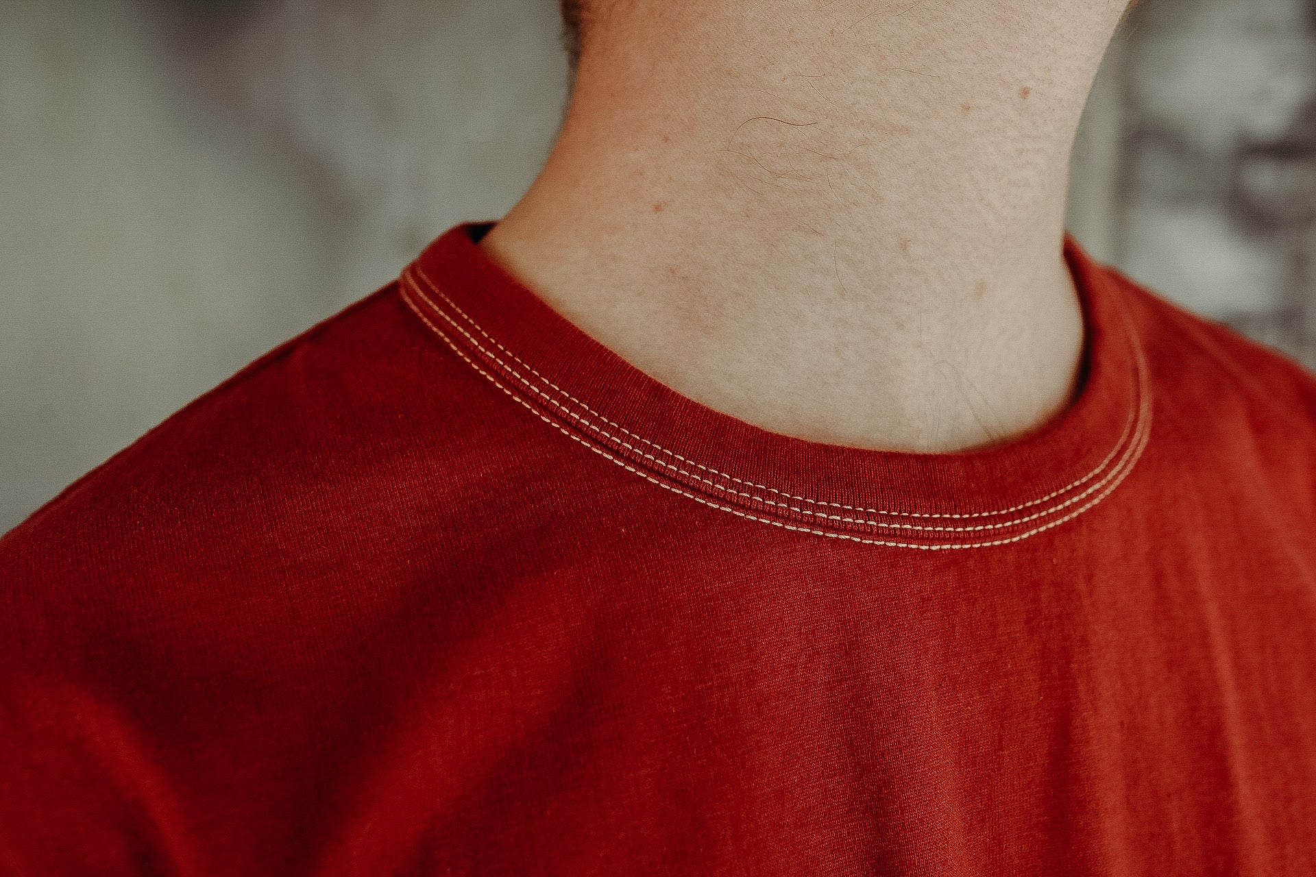 Close-up of a person wearing a red crew neck T-shirt with visible double-stitching detail from Iron Shop Provisions