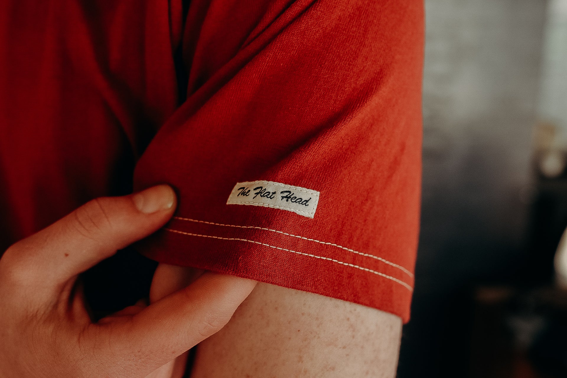 Close-up of red short sleeve shirt with 'The Flat Head' label and hand holding the fabric