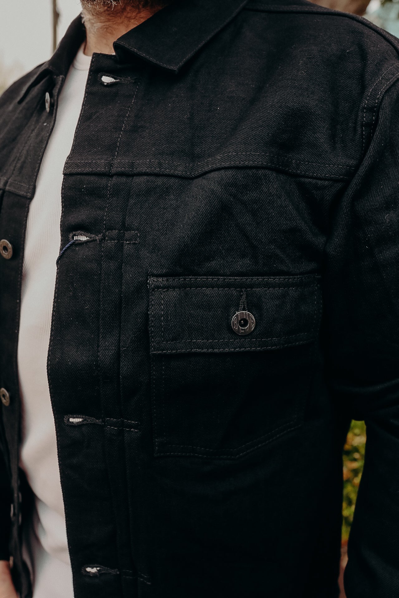 Close-up of a man wearing a black rugged work jacket with buttoned chest pocket over a white t-shirt