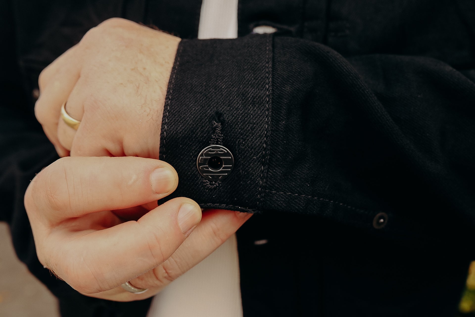 Close-up of hands fastening black denim jacket cuff with metal button detail at Iron Shop Provisions
