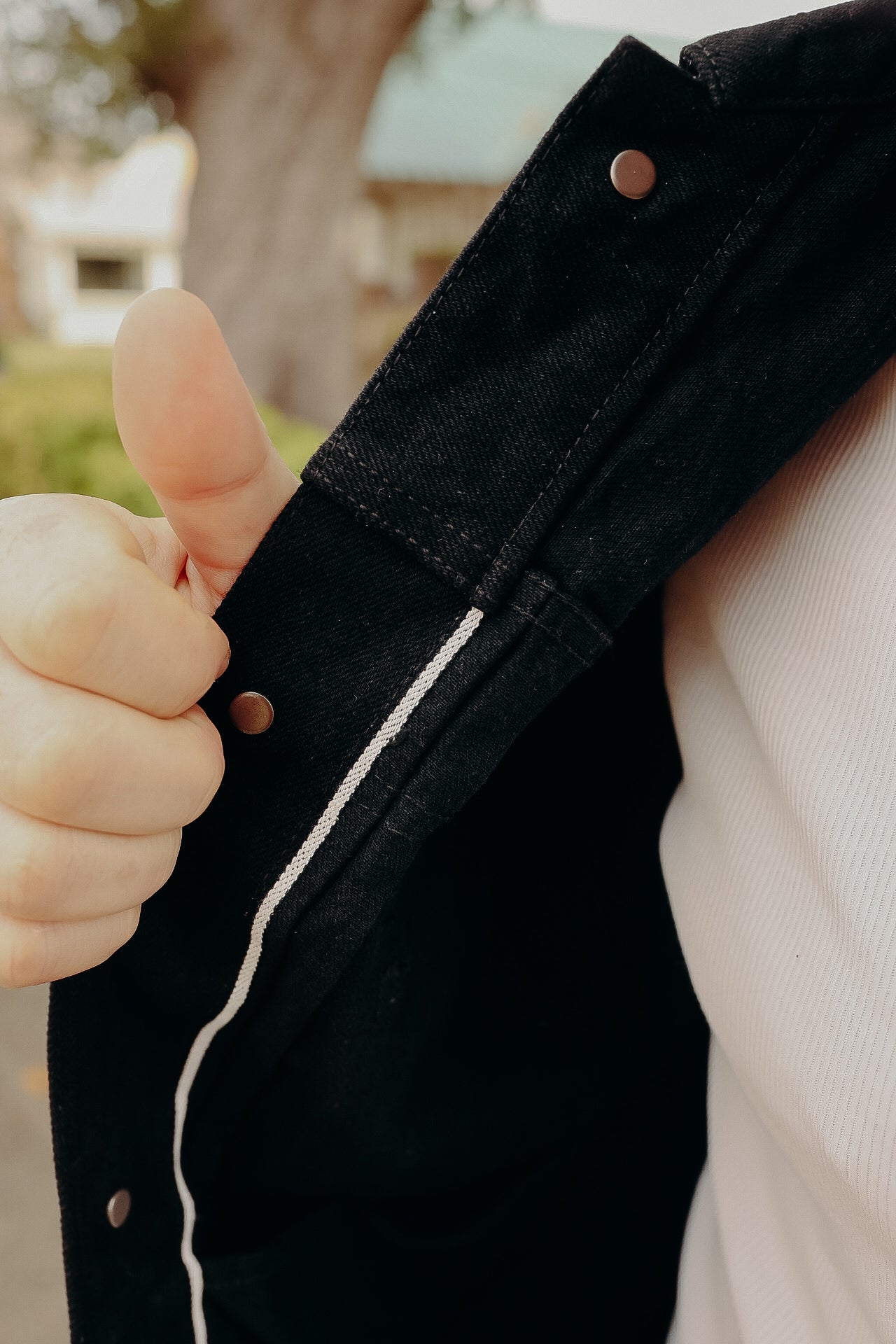Close-up of hand showing thumbs-up next to black denim jacket with white stitching detail