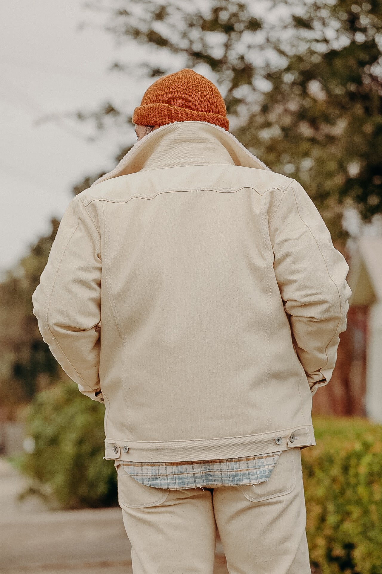 Man wearing beige work jacket and pants with orange knit beanie outdoors in fall setting