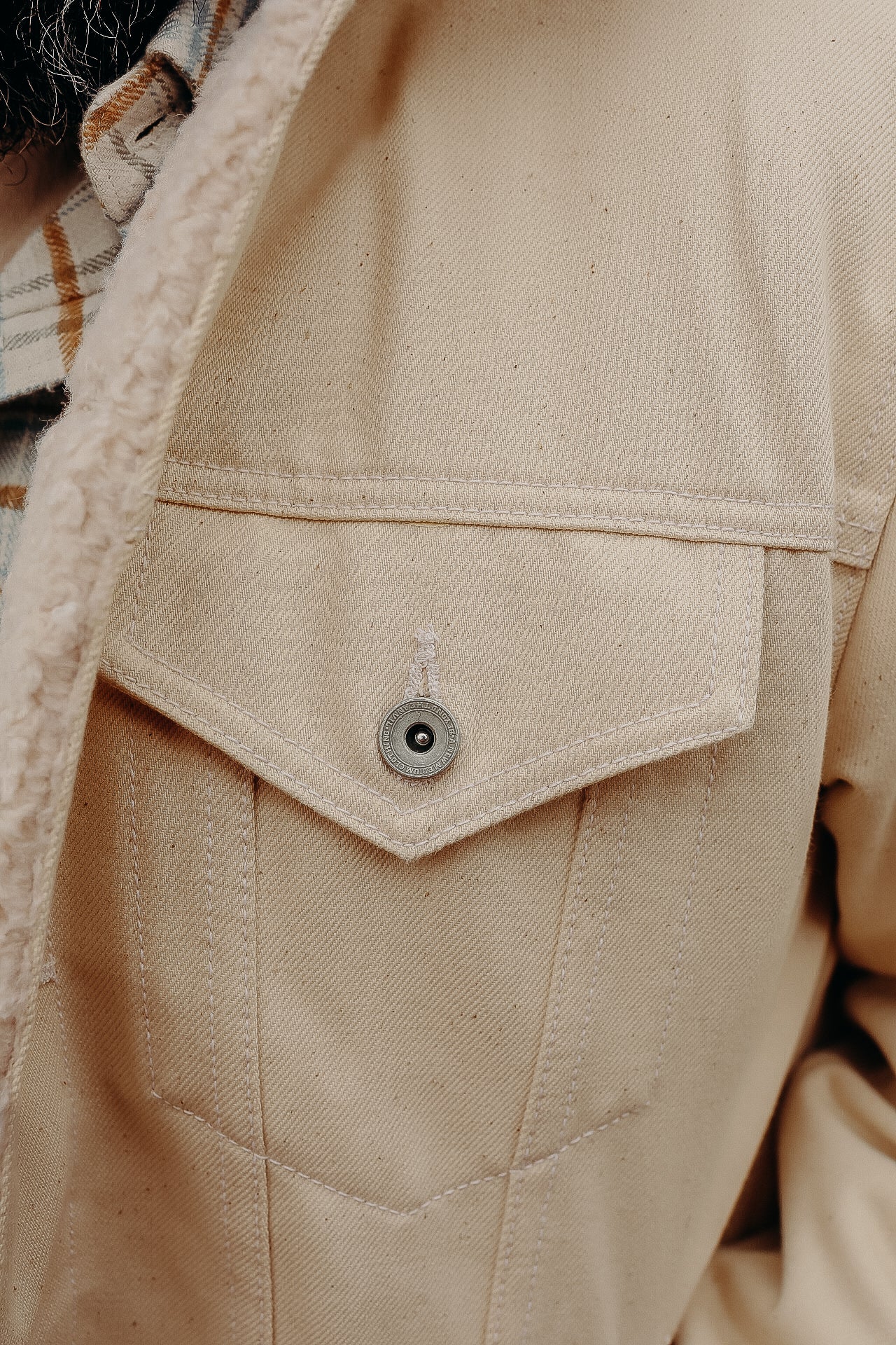 Close-up of beige canvas jacket pocket with metal button and visible stitching detail