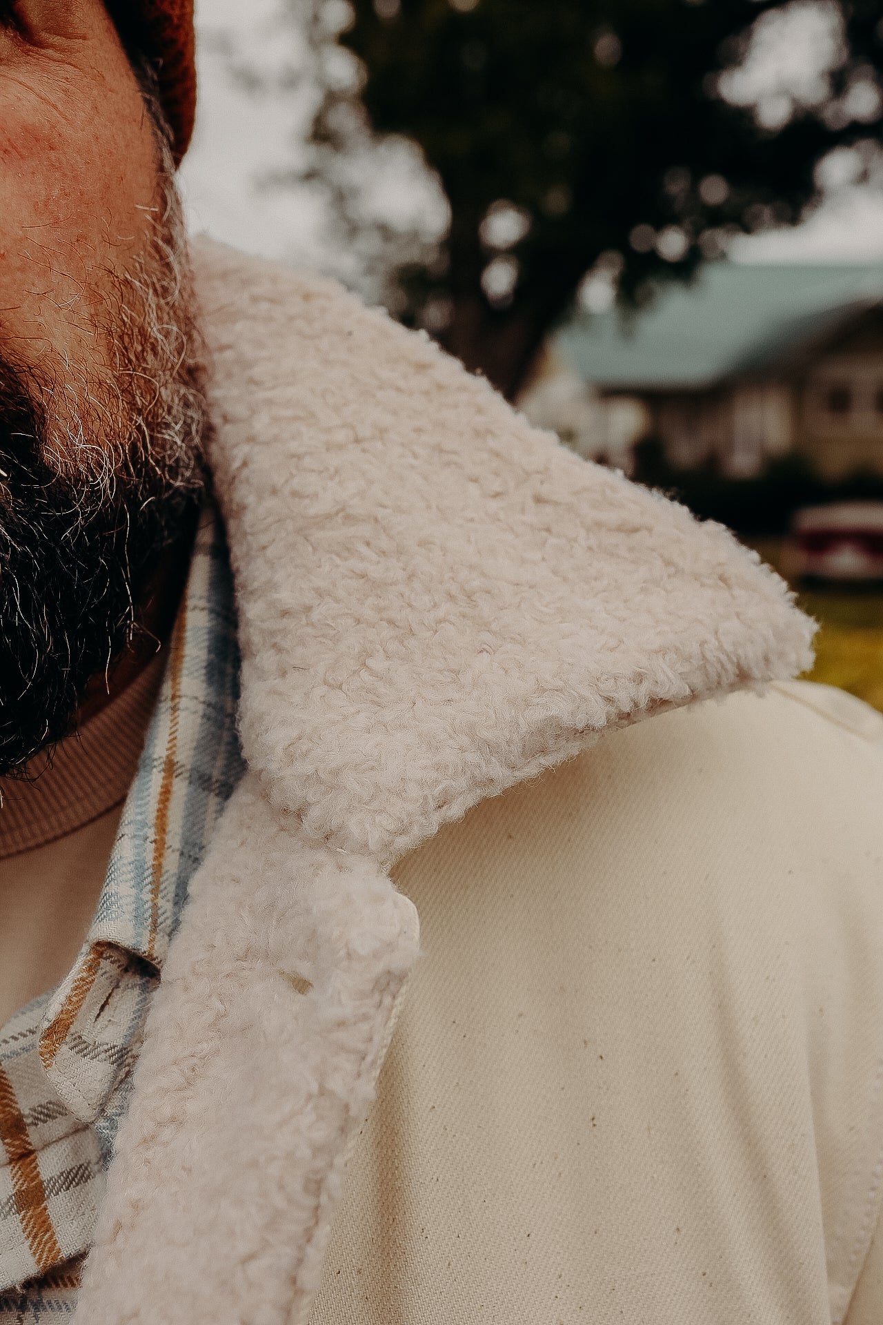 Close-up of warm shearling collar on beige jacket worn over plaid shirt and brown sweater outdoors