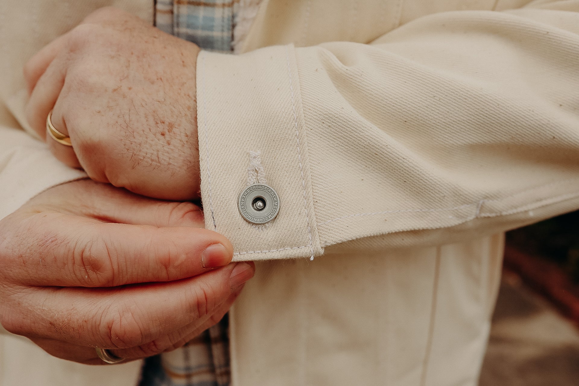 Close-up of a person adjusting the cuff of a cream-colored work jacket with a metal snap button at Iron Shop Provisions