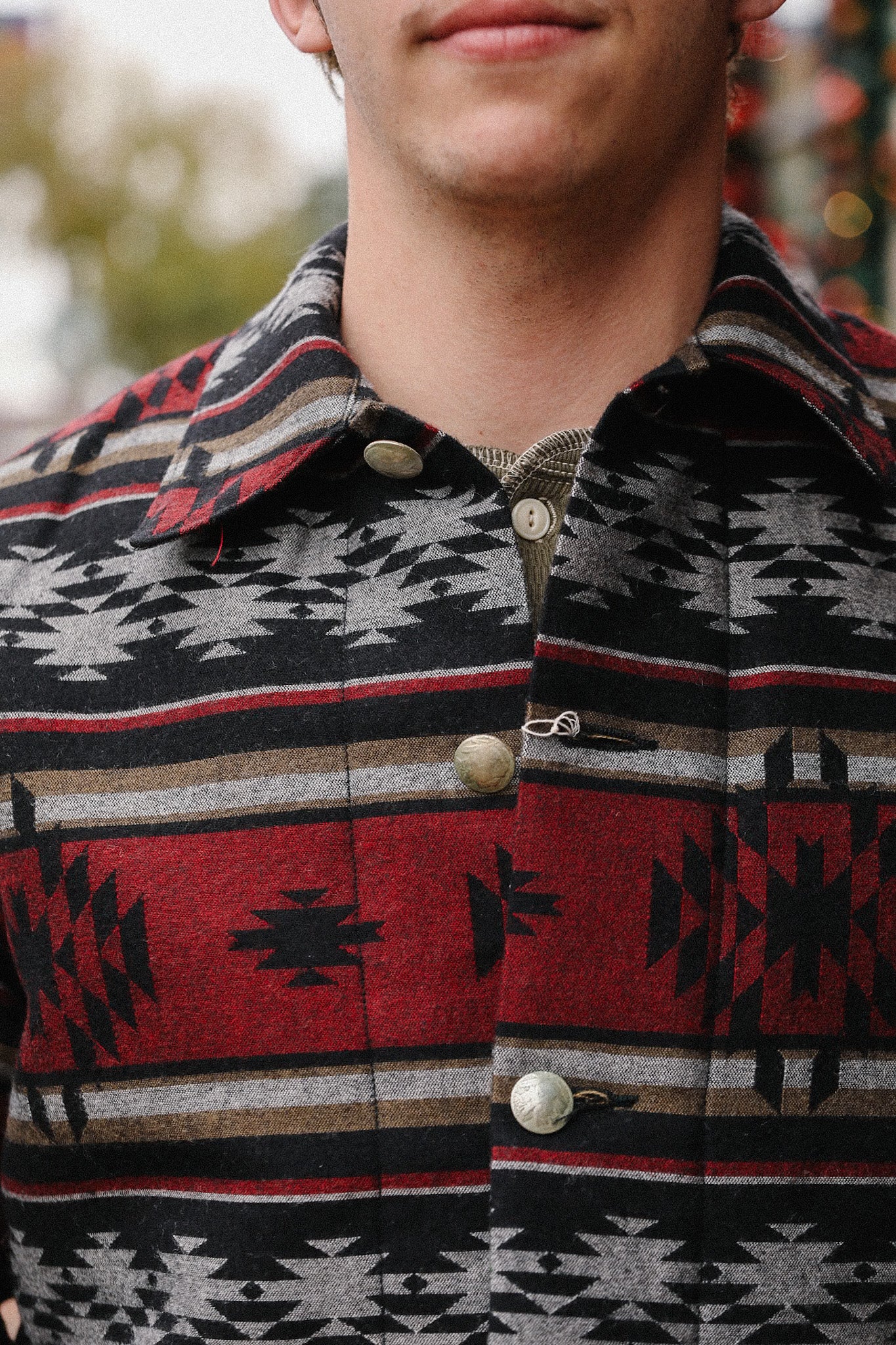 Close-up of a man wearing a red and black Native American patterned shirt jacket with metal buttons