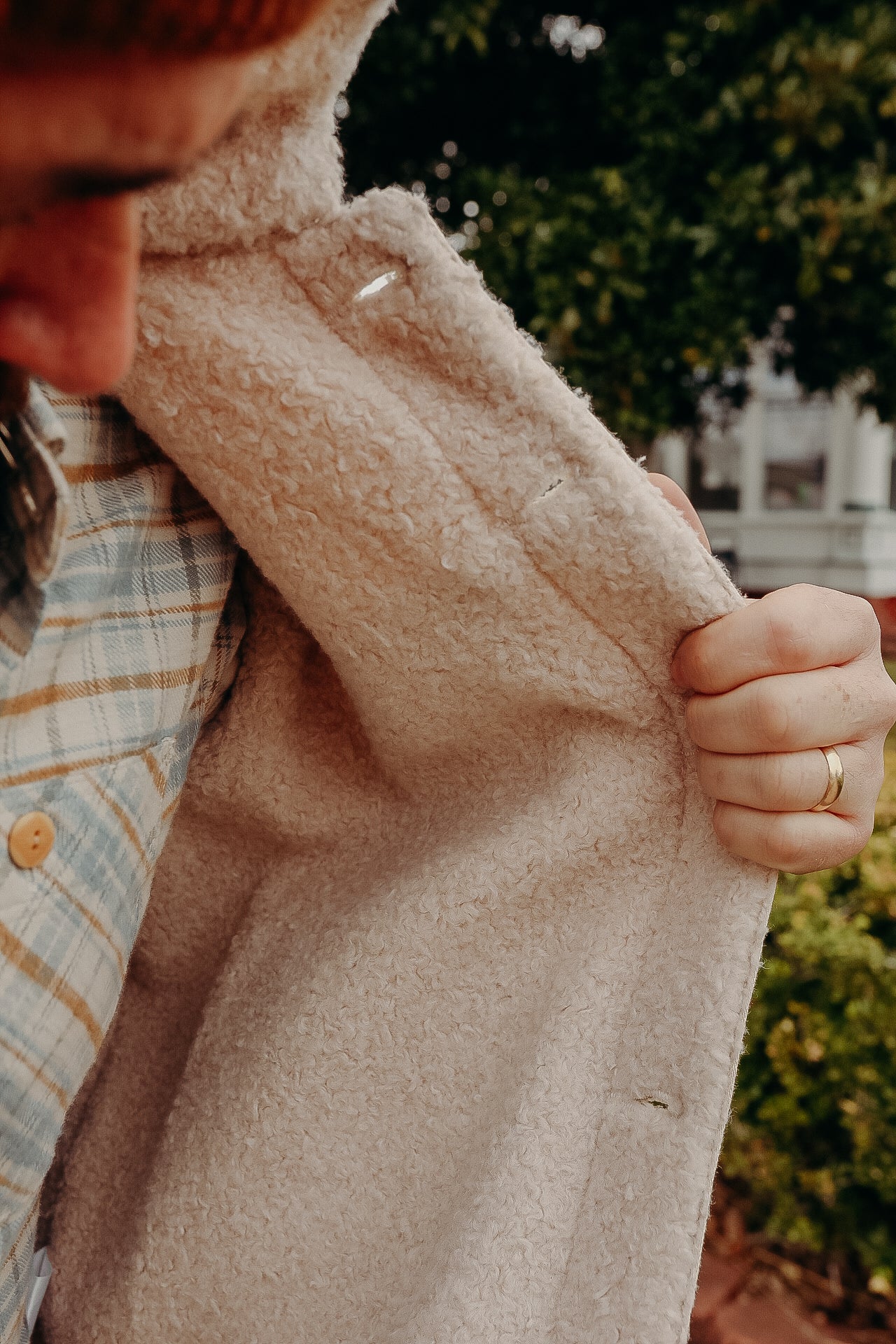Close-up of person holding open soft beige sherpa jacket revealing cozy texture over plaid shirt outdoors