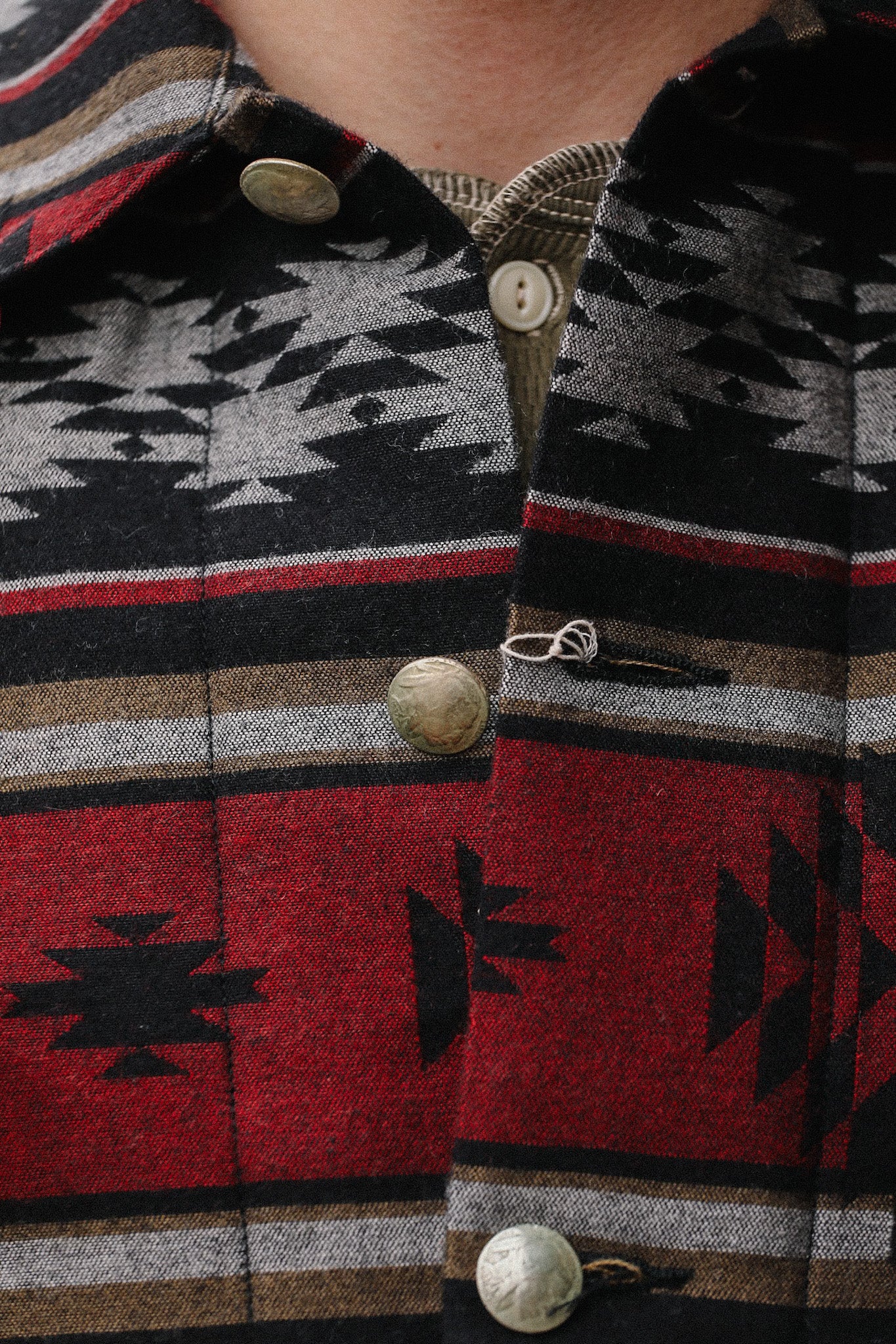 Close-up of a jacket with Native American-inspired geometric patterns, metal buttons, and layered beige shirt