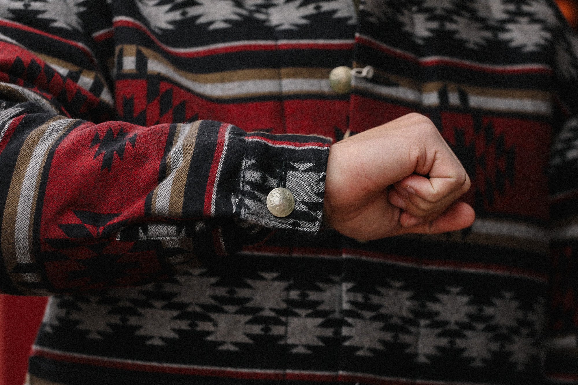 Close-up of arm in Native American inspired patterned jacket with silver snap button cuff, rustic red and black colors