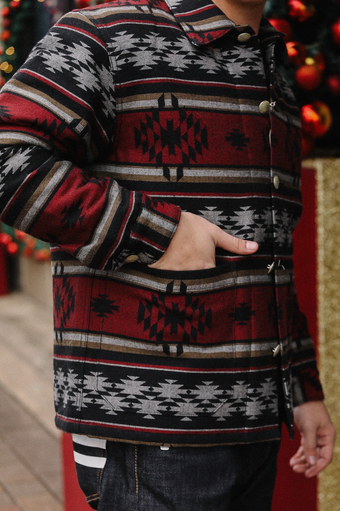 Close-up of a person wearing a patterned red, black, and gray jacket with geometric prints, hand in pocket