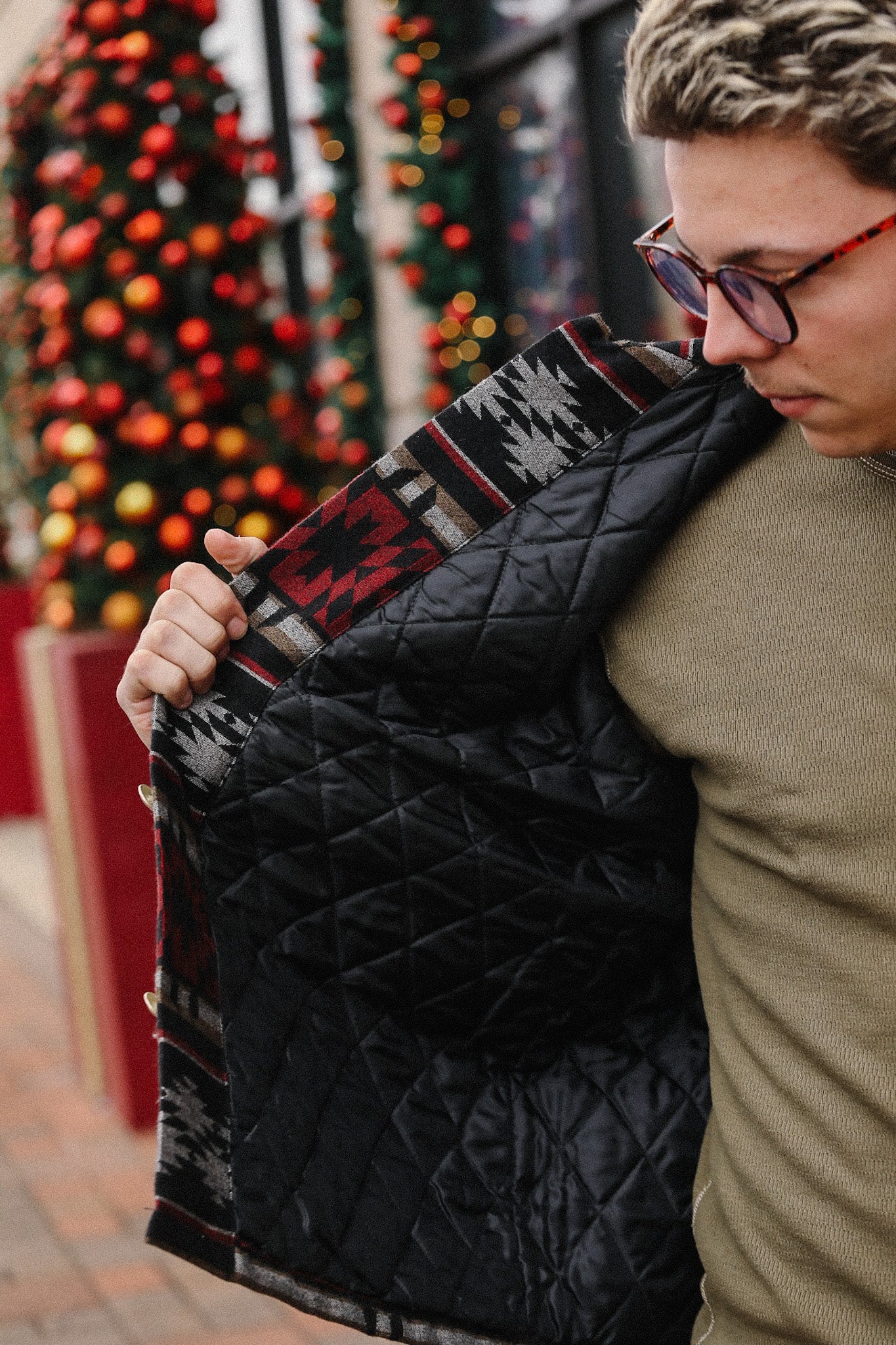 Man wearing patterned jacket with quilted black lining next to decorated Christmas trees outdoors