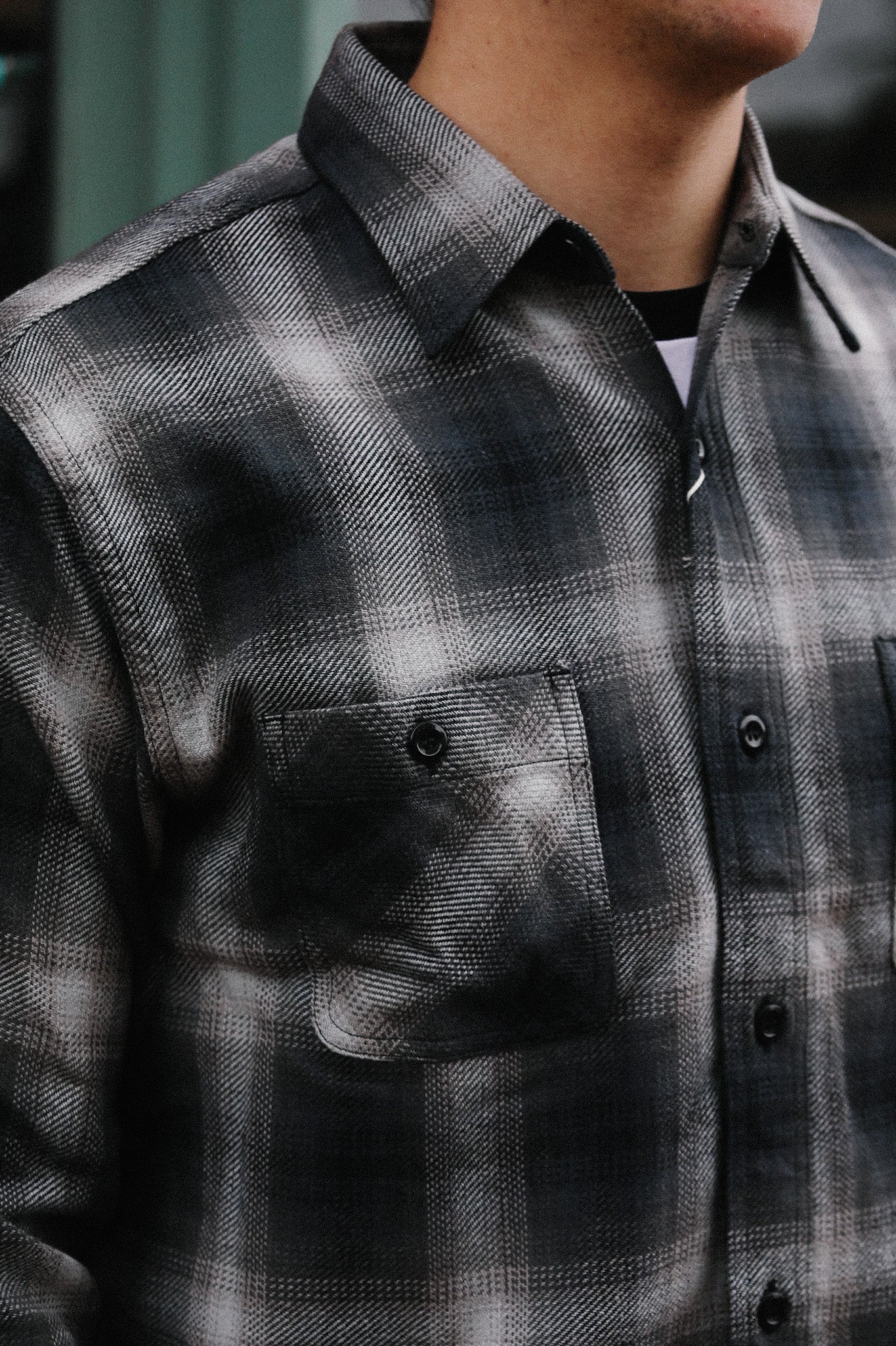 Close-up of a man wearing a black and gray plaid flannel shirt with buttoned chest pockets