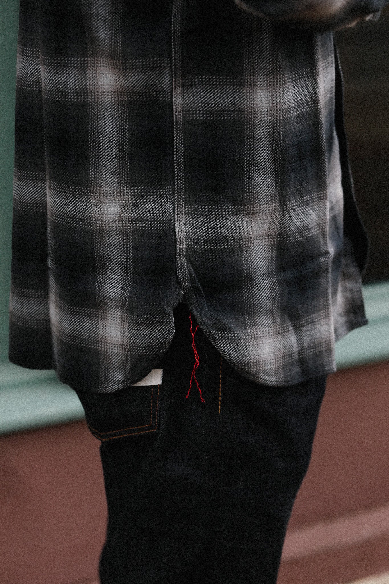 Close-up of black and white plaid shirt hem with red stitching paired with dark denim jeans pocket
