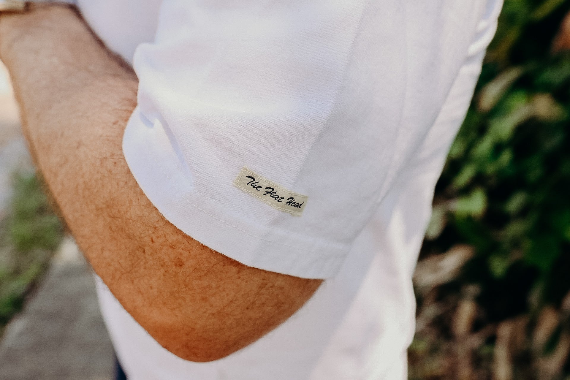 Close-up of a person's arm wearing a white shirt with a 'The Flexi Head' tag on the sleeve, outdoors