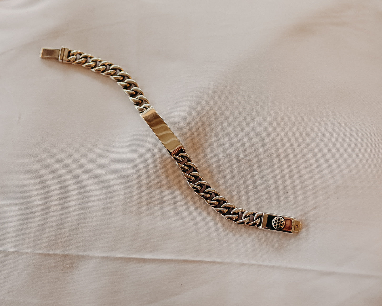 Silver chain bracelet with solid plate and floral clasp detail on white fabric