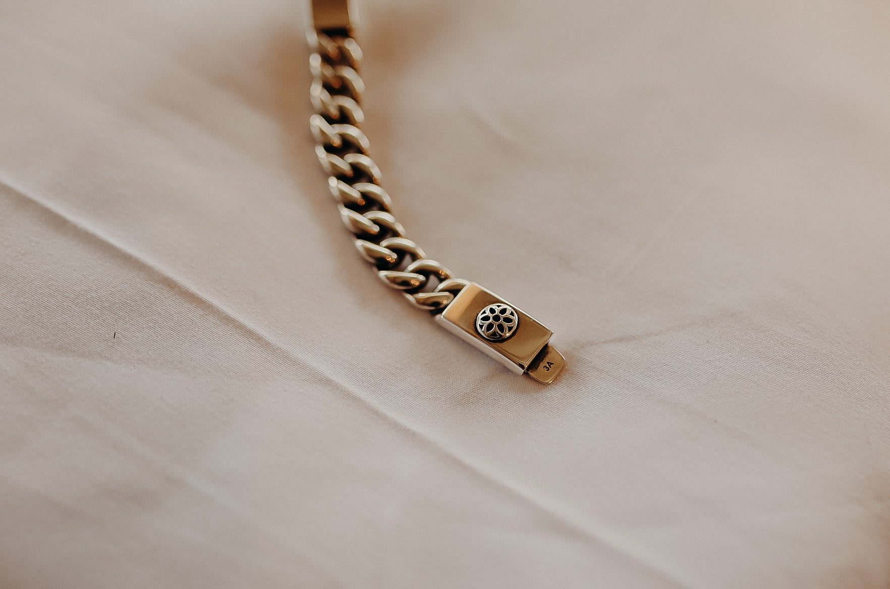 Close-up of a silver chain bracelet with a decorative clasp resting on beige fabric
