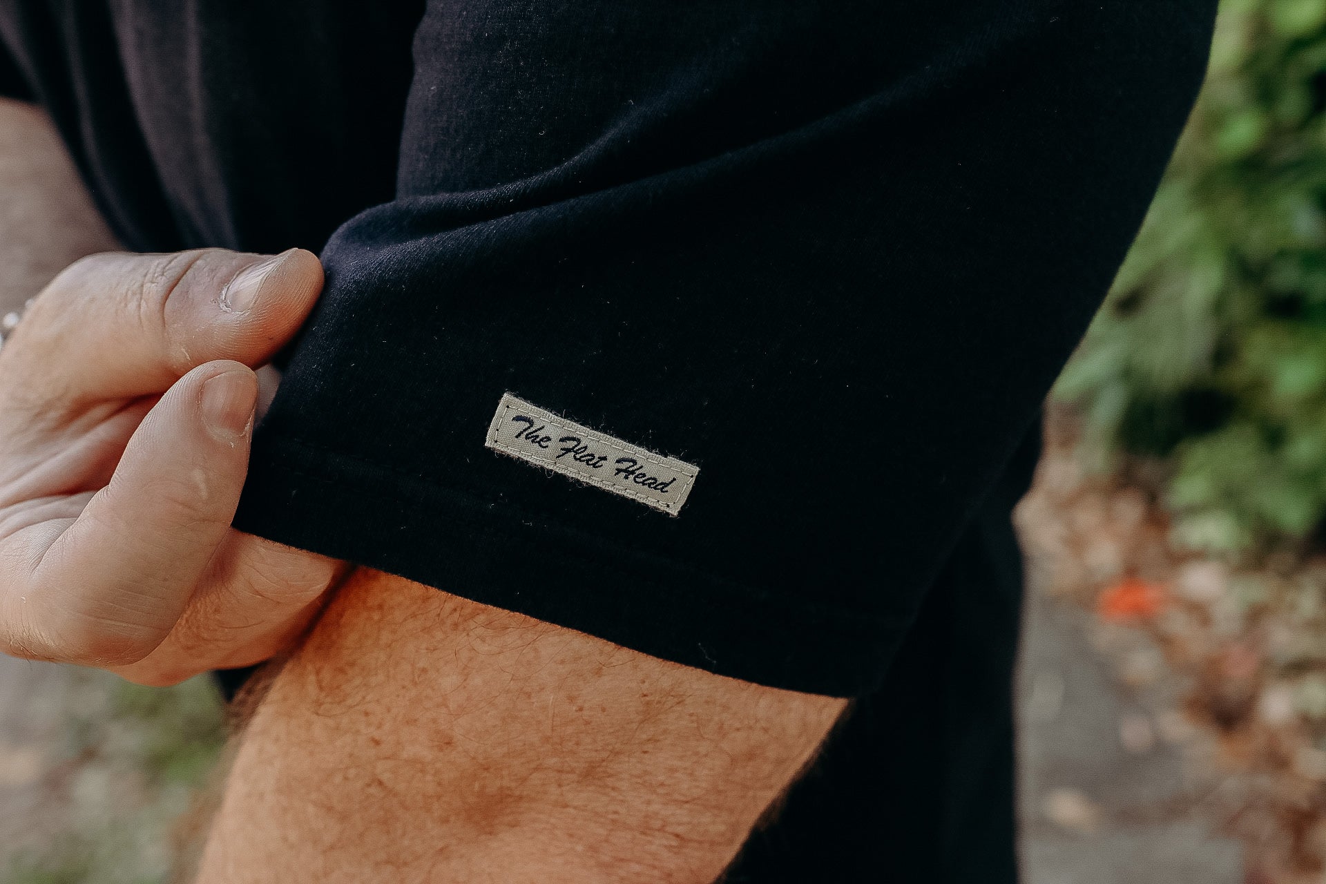 Close-up of a man's arm wearing a black short sleeve shirt with a small fabric label reading 'The Flat Head'