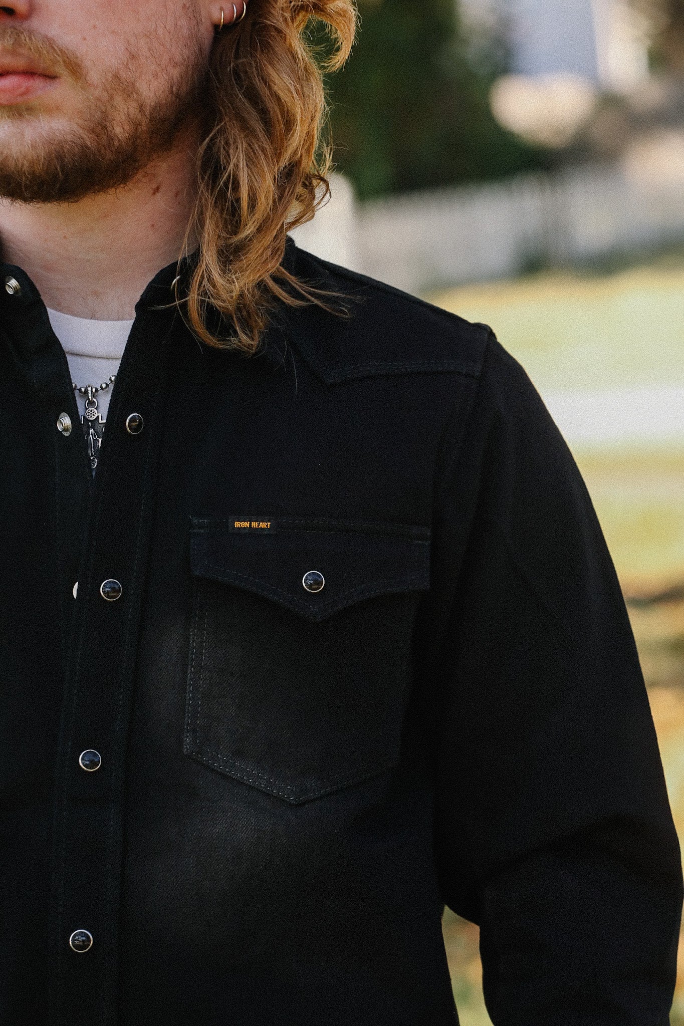 Close-up of a man wearing a black Iron Heart denim jacket with snap buttons and chest pocket outdoors