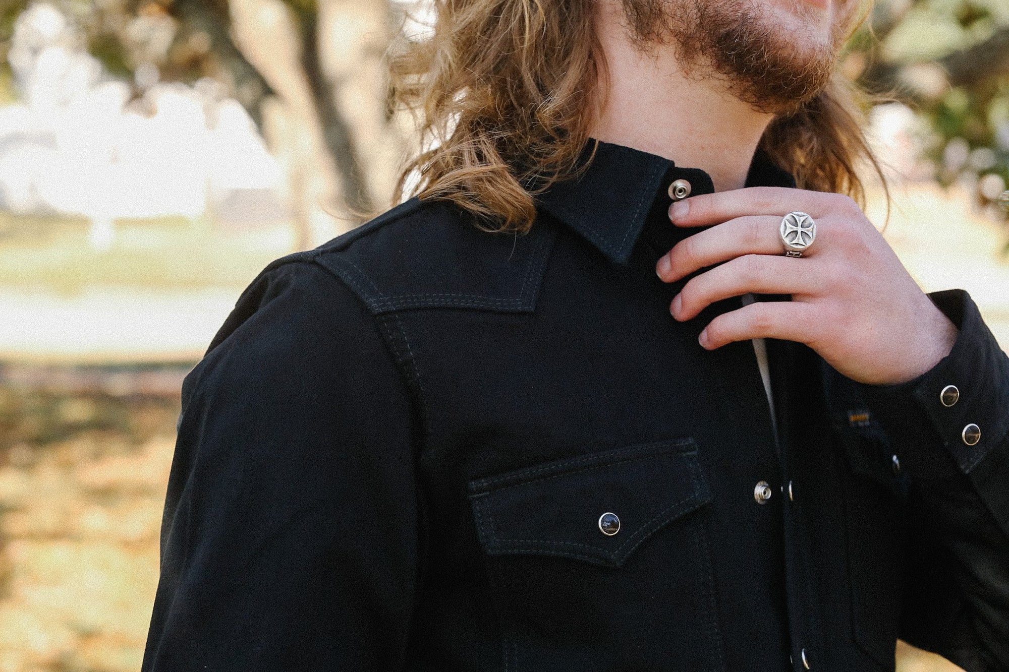Close-up of person in black denim jacket with silver snap buttons and silver iron cross ring outdoors