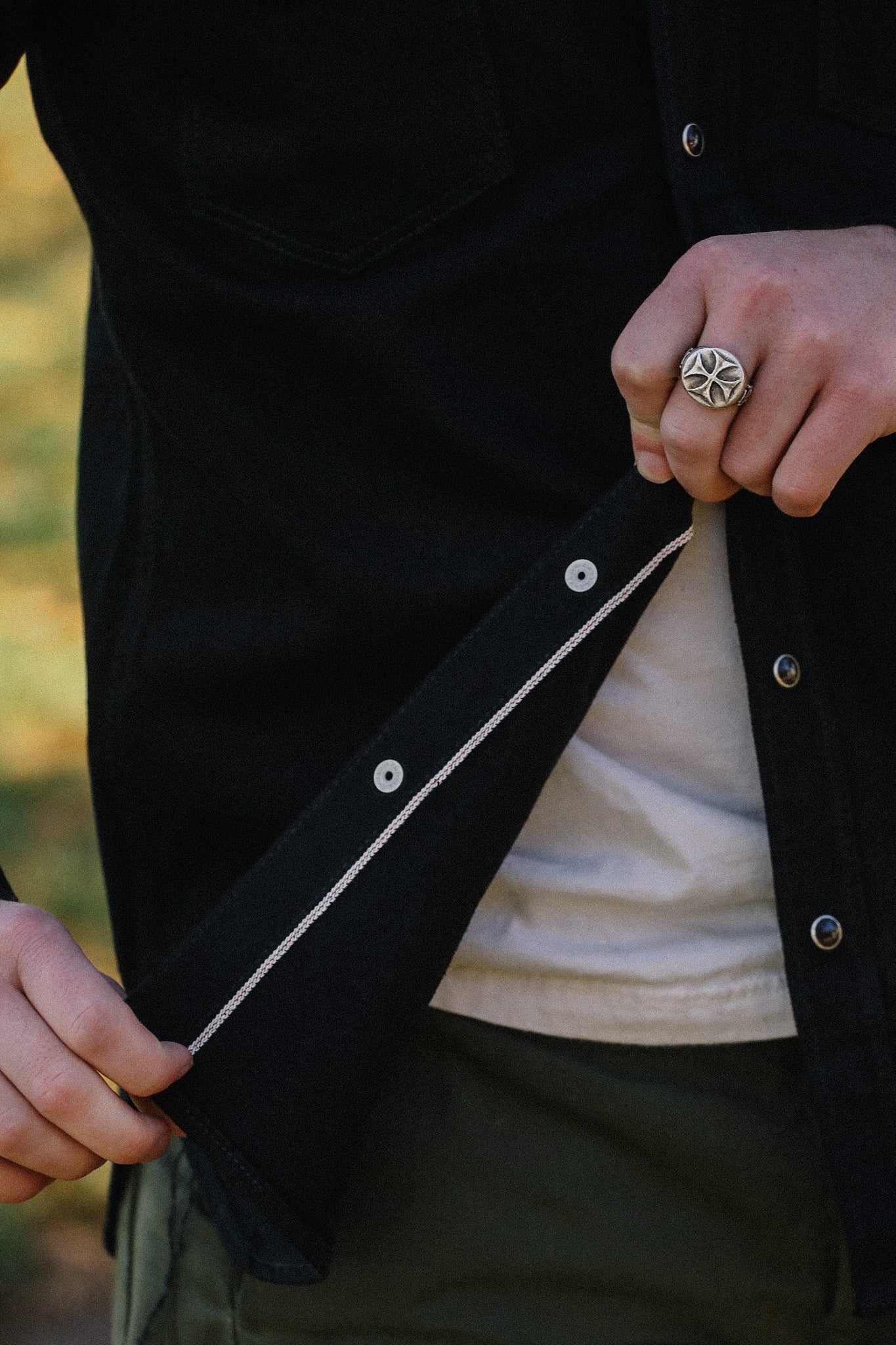 Close-up of a person wearing a black shirt with snap buttons, showing detailed stitching, and a ring on their finger