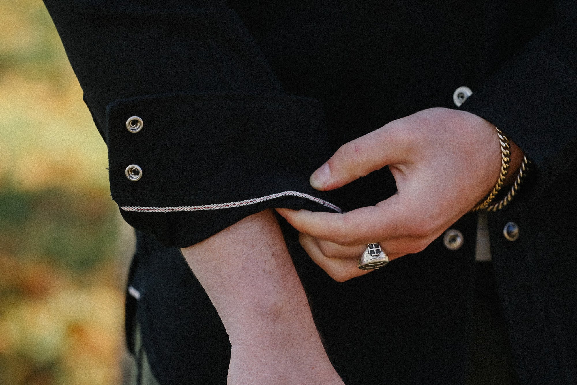Close-up of a person rolling up the sleeve of a black denim jacket with silver buttons and white stitching at Iron Shop Provisions