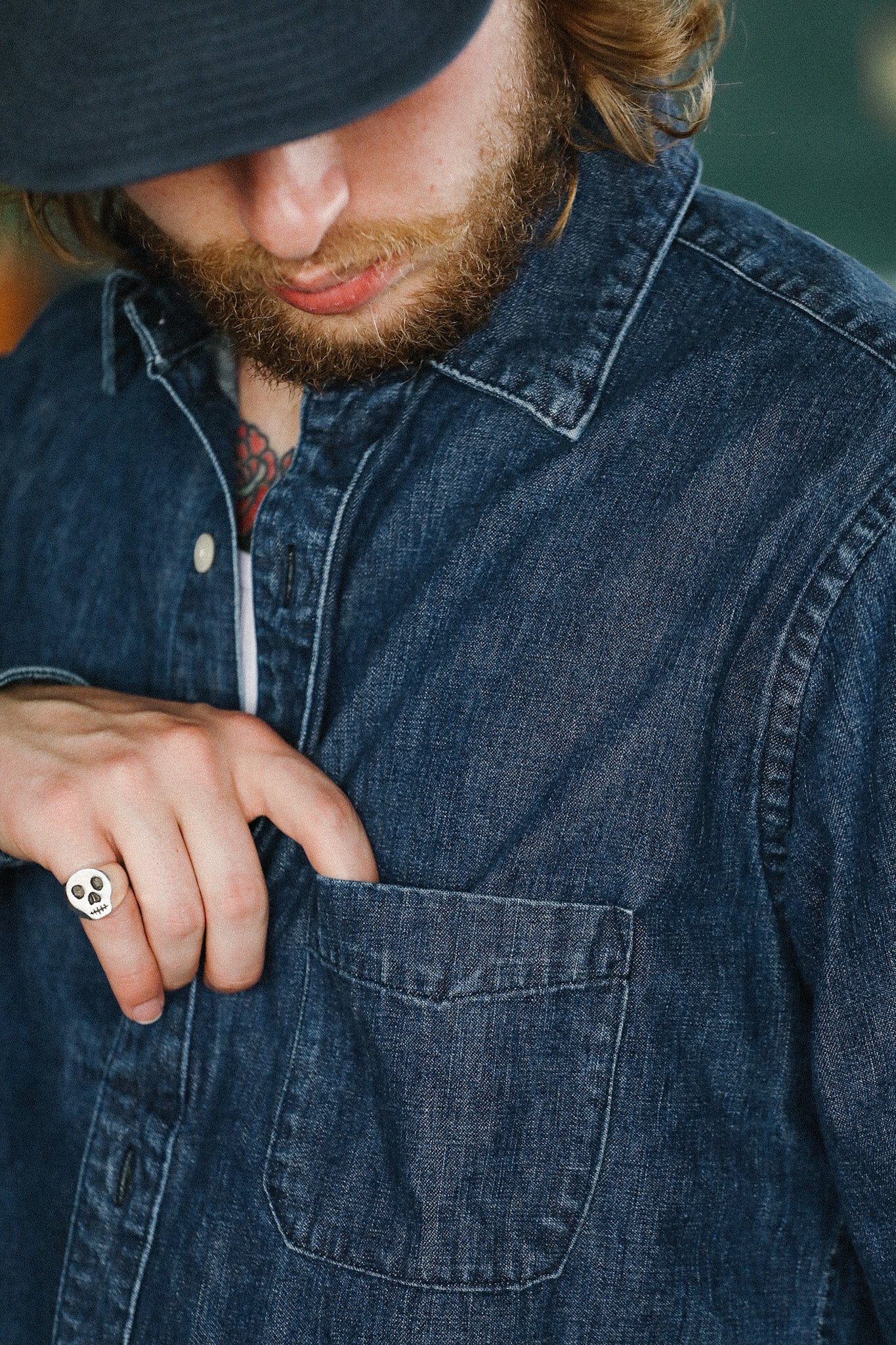 Man in dark denim shirt with skull ring on finger reaching into chest pocket