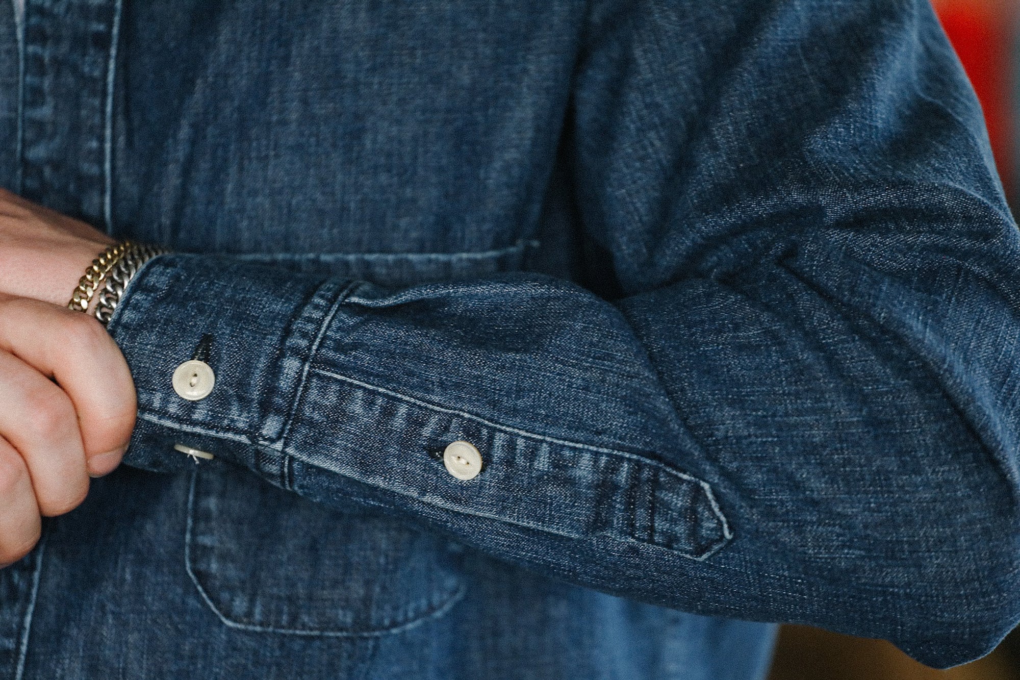 Close-up of person wearing a dark denim shirt with white buttons and silver bracelets on wrist