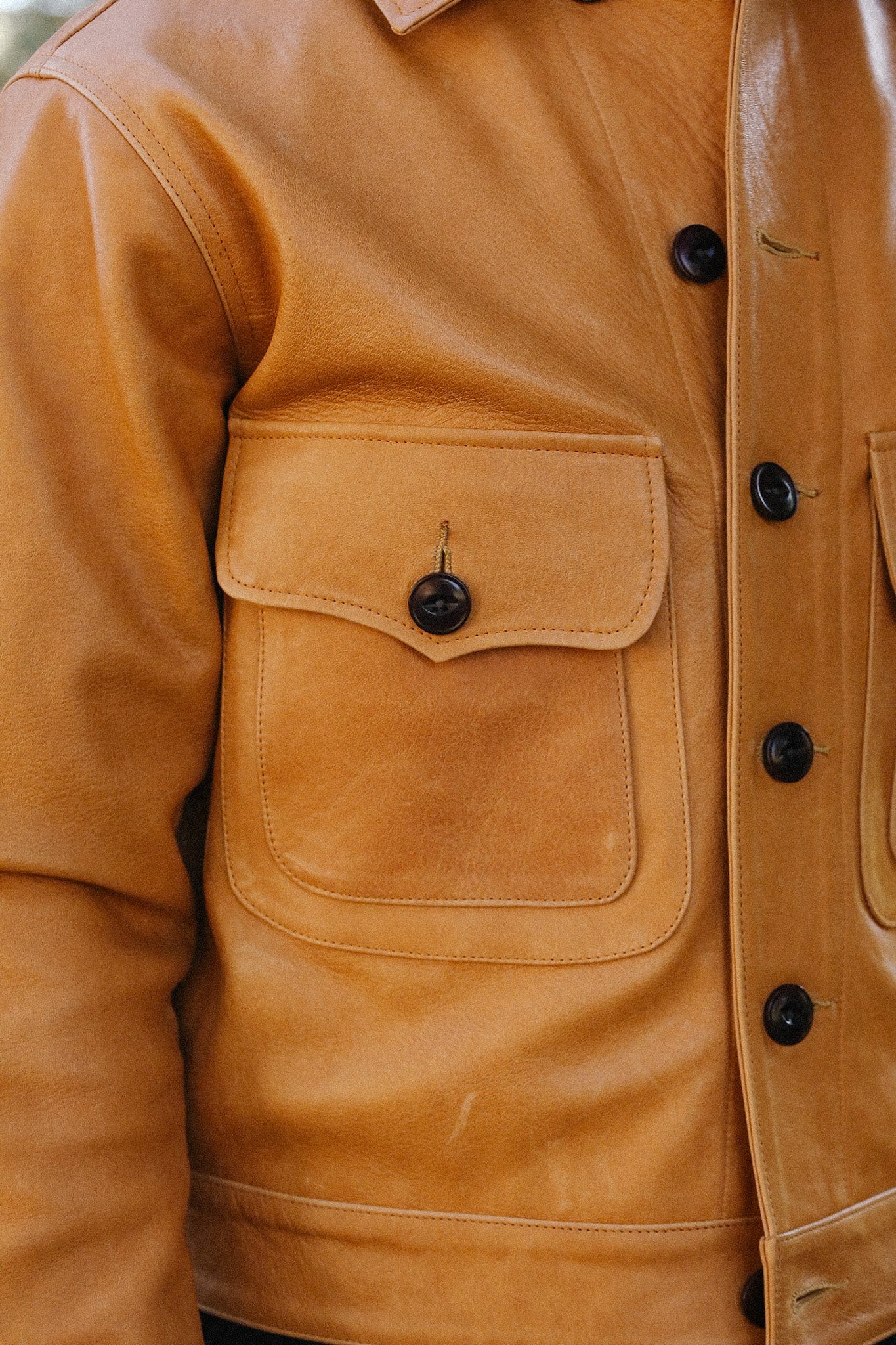 Close-up of tan leather jacket pocket with black button and detailed stitching from Iron Shop Provisions