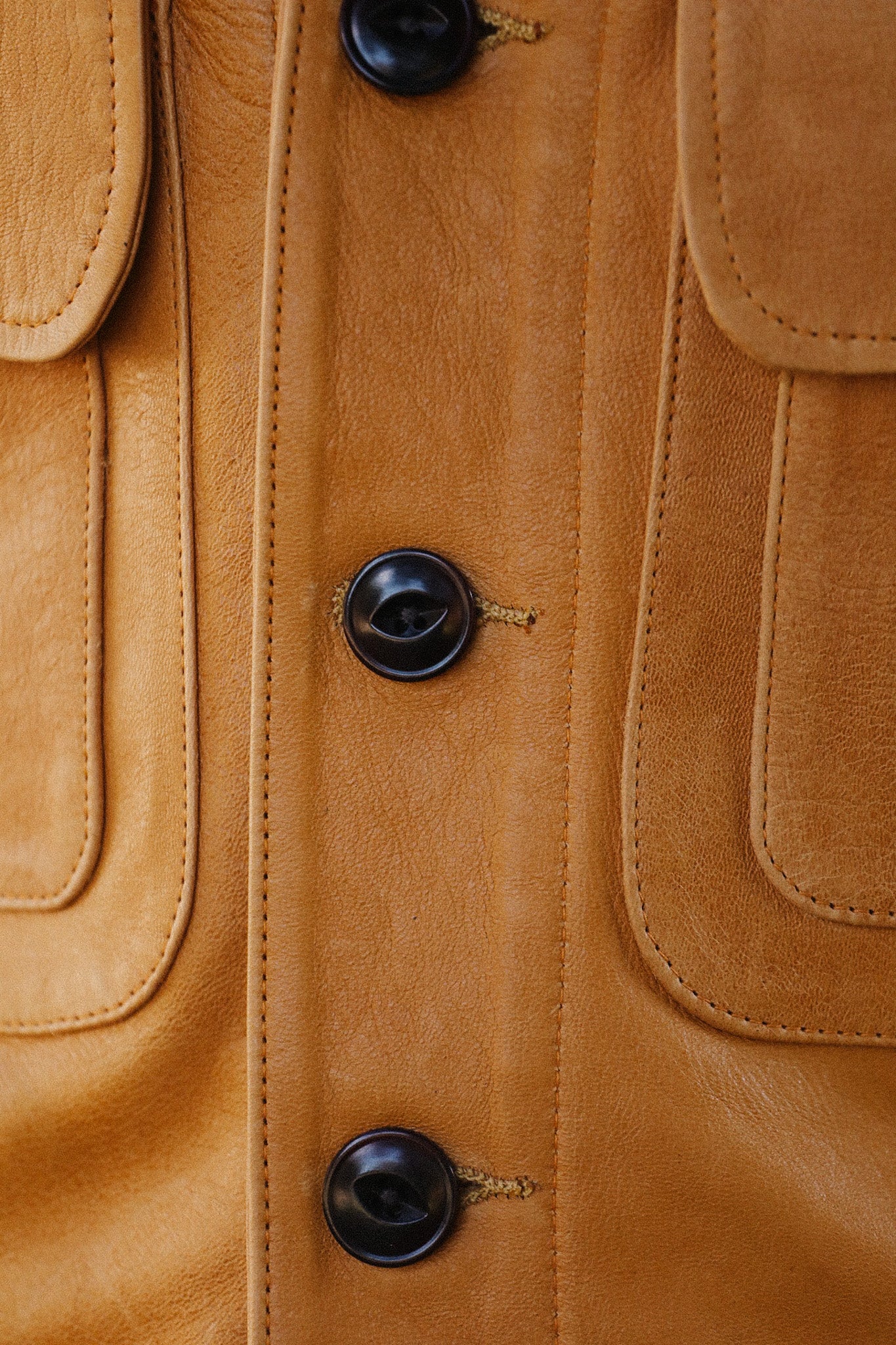 Close-up of tan leather jacket with dark buttons and detailed stitching on pockets