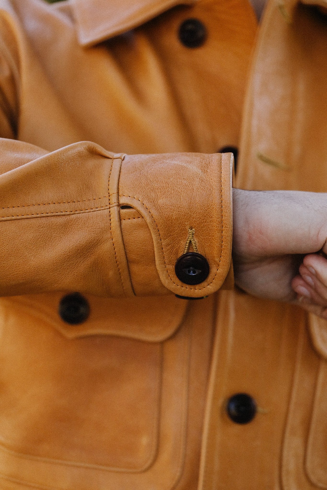 Close-up of a tan leather jacket sleeve with black button detail on cuff and front pocket