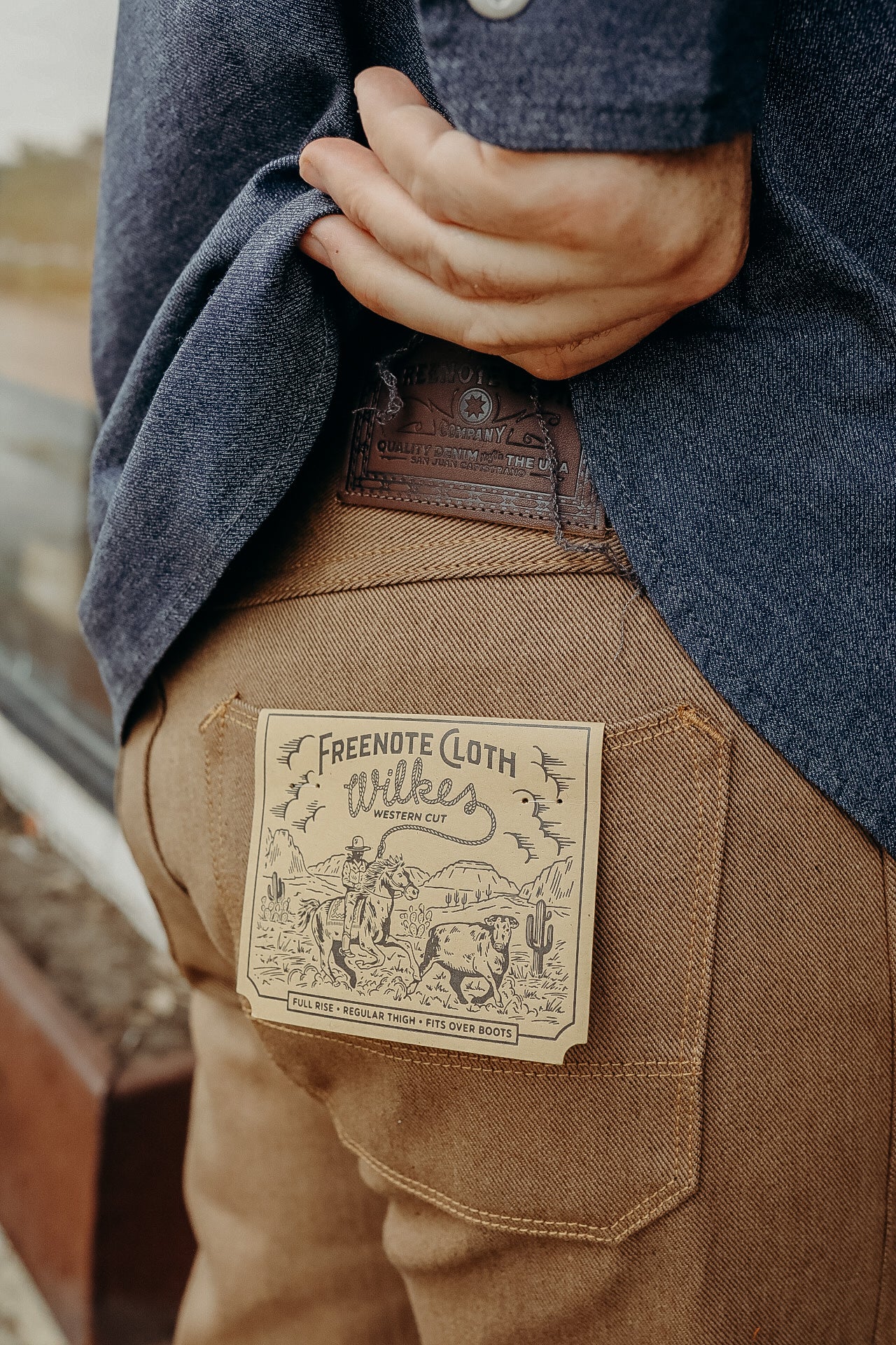 Close-up of tan Freenote Cloth Wilkes Western Cut work pants with cowboy graphic label on back pocket